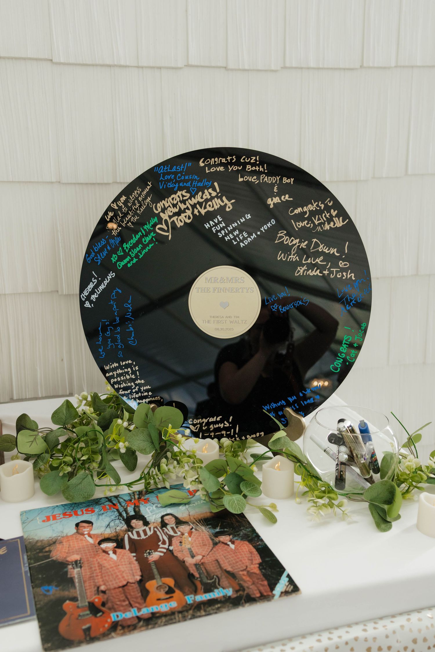 Black vinyl record guest book signed with colorful messages displayed at a wedding reception with greenery decor.