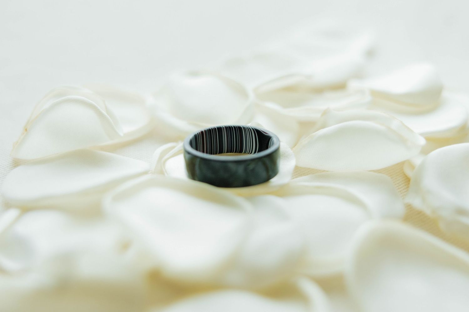 Dark carbon fiber wedding band resting on white flower petals close-up.