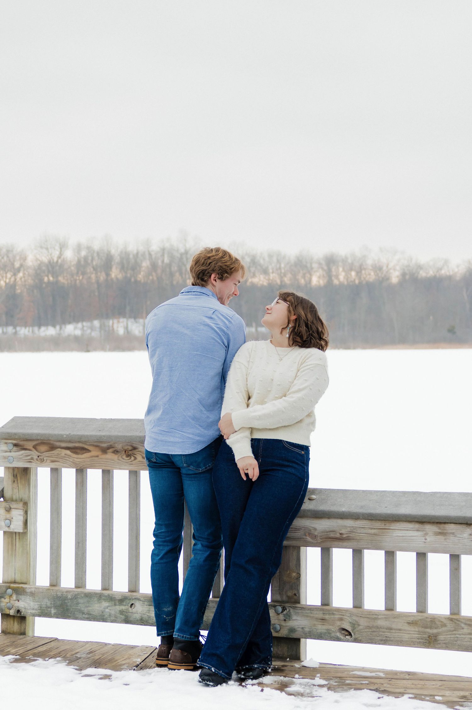 Couple gazing at each other on a wooden dock overlooking a frozen winter lake.