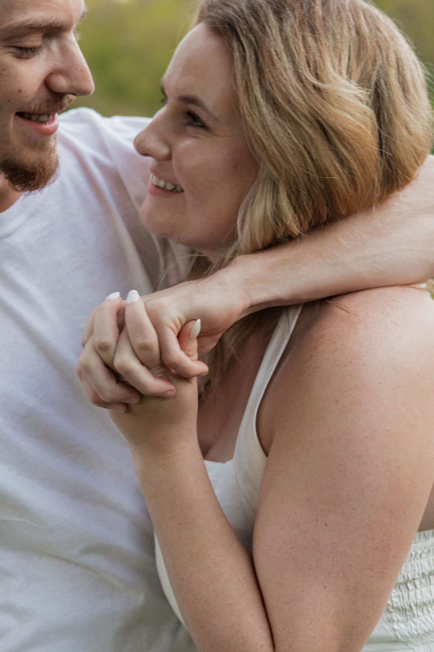 Joyful couple holding hands and smiling at each other outdoors in a natural setting.