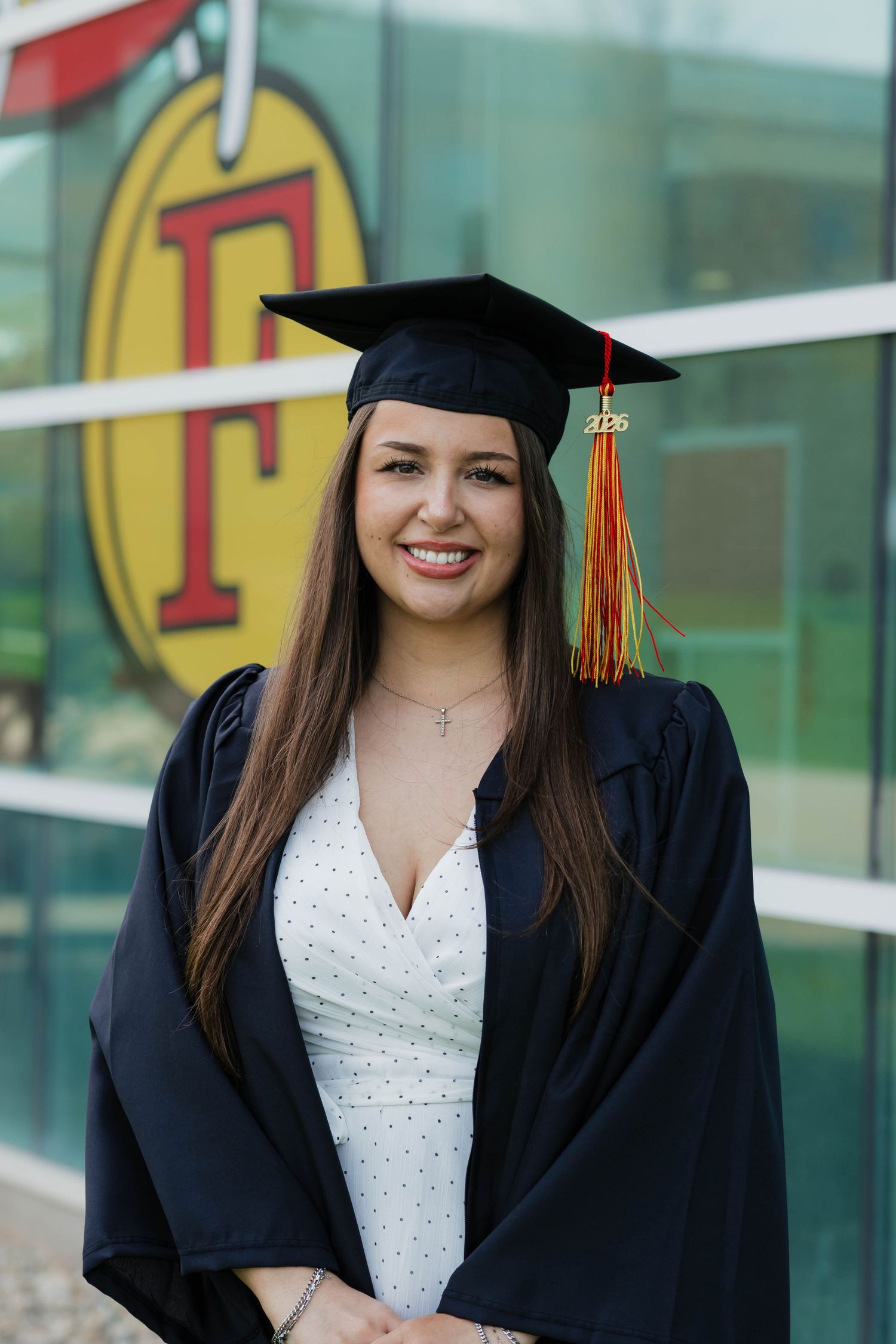 Smiling female graduate in black cap and gown posing in front of Ferris State University logo.