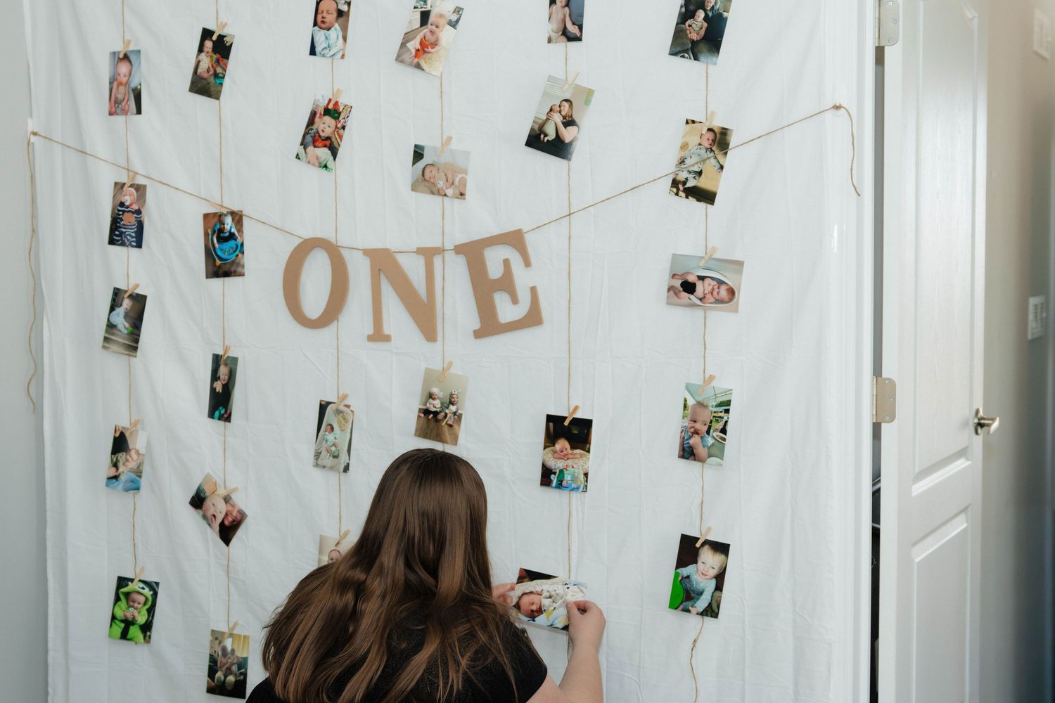 Woman arranging a photo display wall with ONE banner for a first birthday party celebration.
