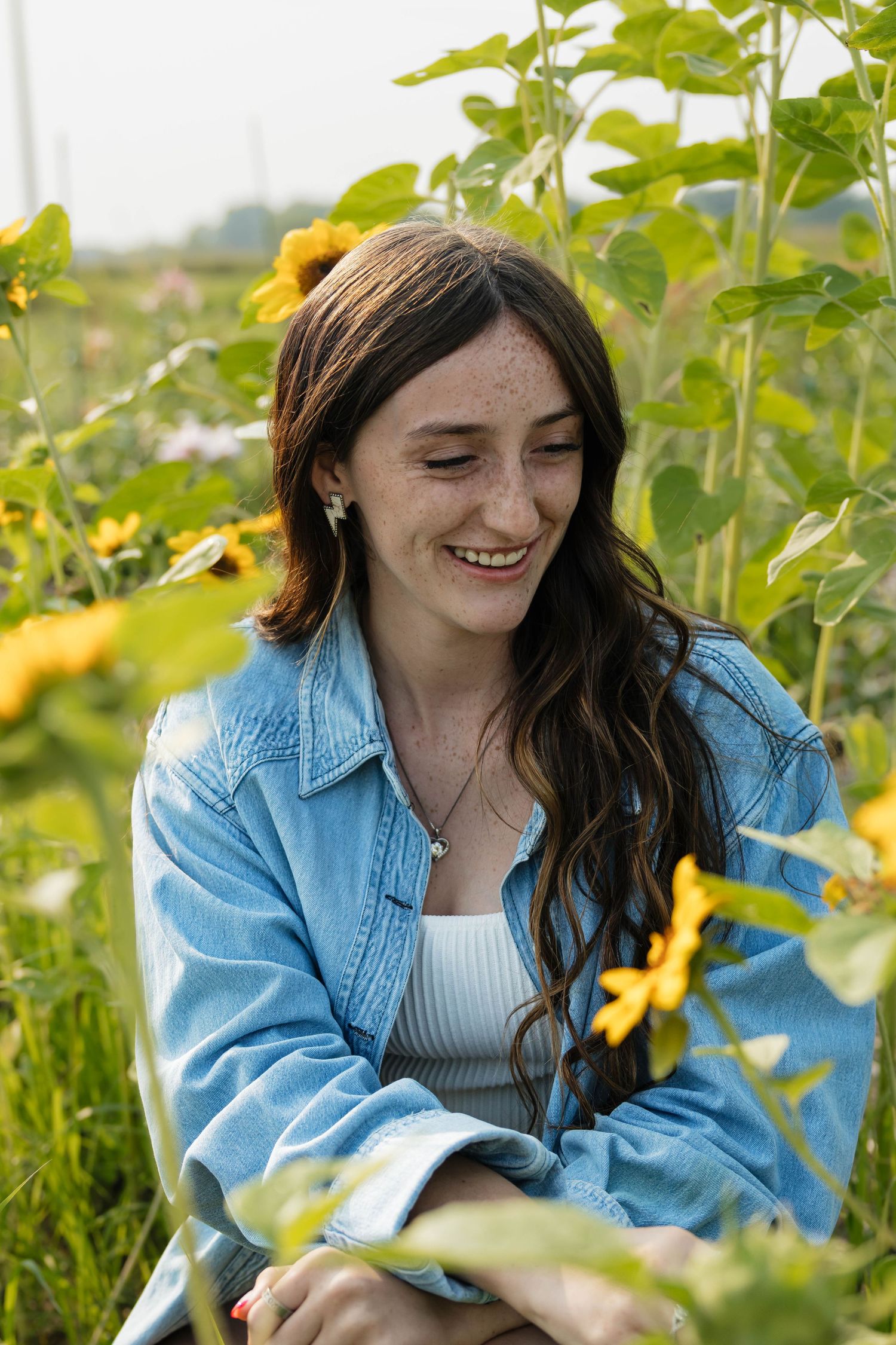 Smiling brunette teen with freckles among sunflowers in field.