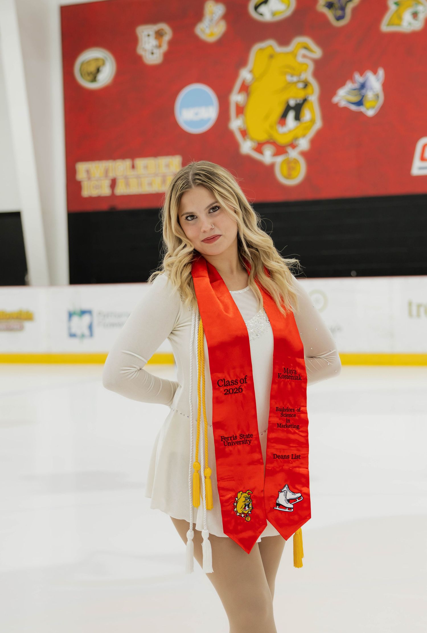 Graduate on ice rink wearing white dress and Ferris State University red graduation stole.