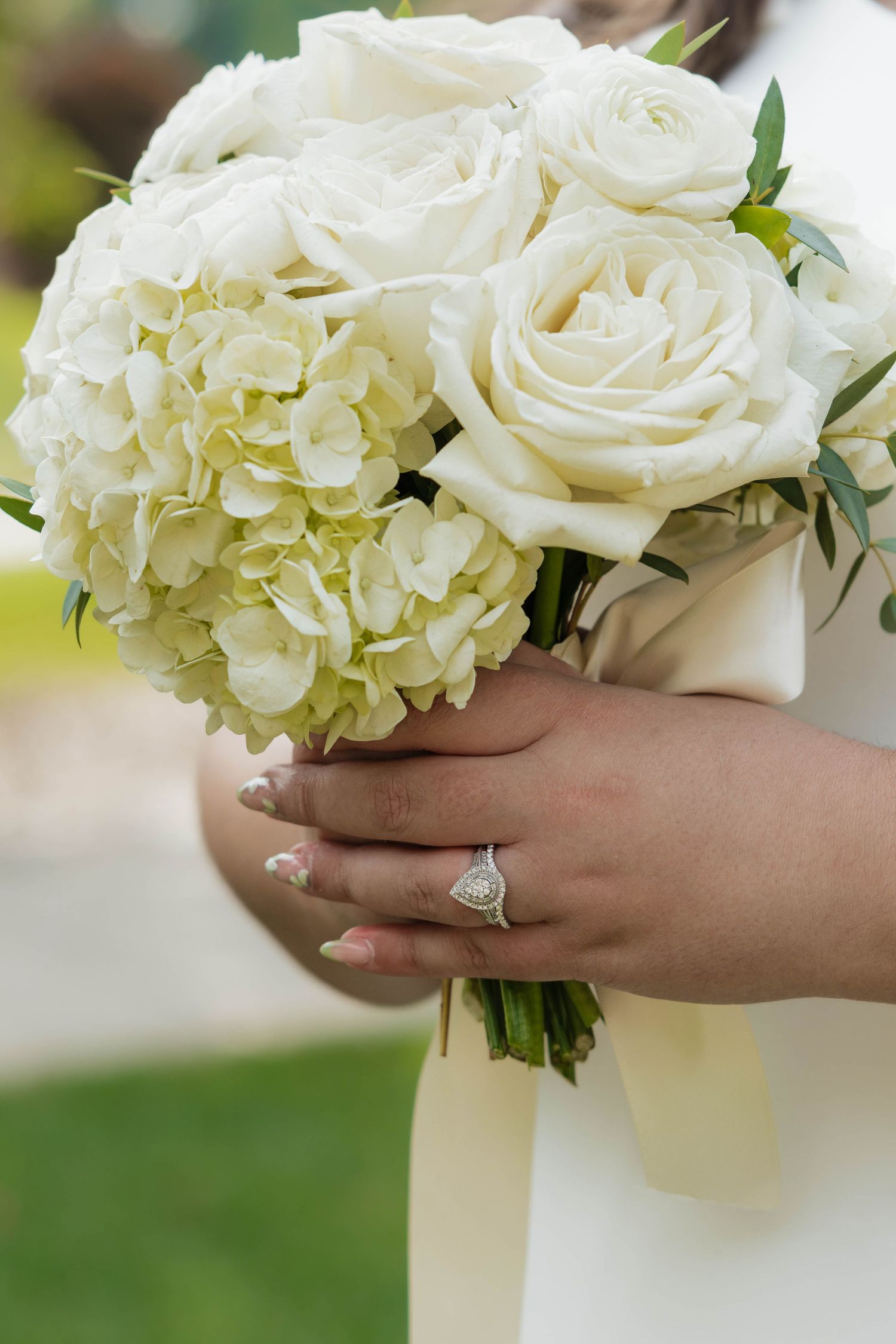 Bride holding beautiful white rose and hydrangea bouquet with diamond engagement ring detail.
