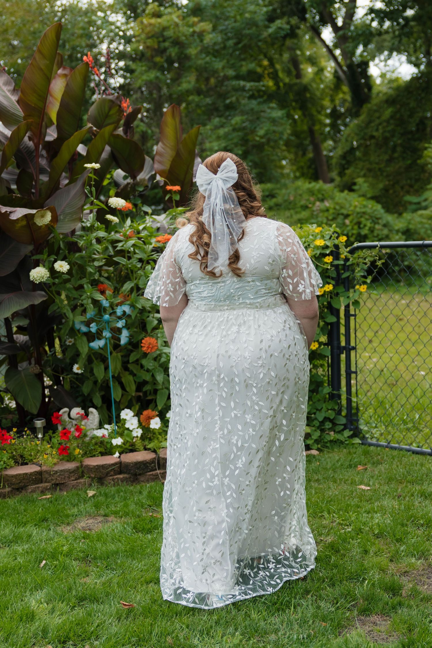 Back view of bride in white embroidered wedding dress with bow veil in flower garden.
