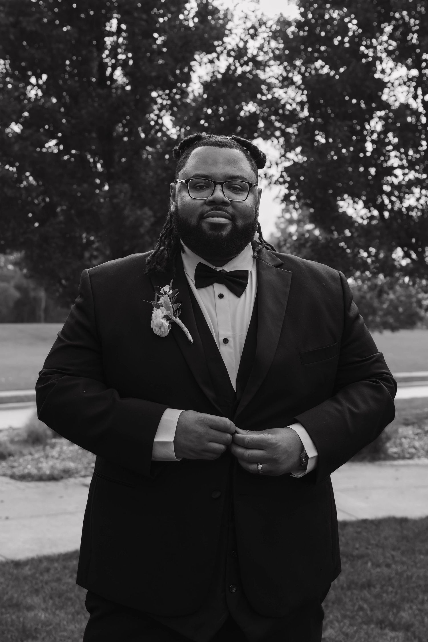 Black and white portrait of groom in tuxedo with boutonniere posing outdoors at wedding.