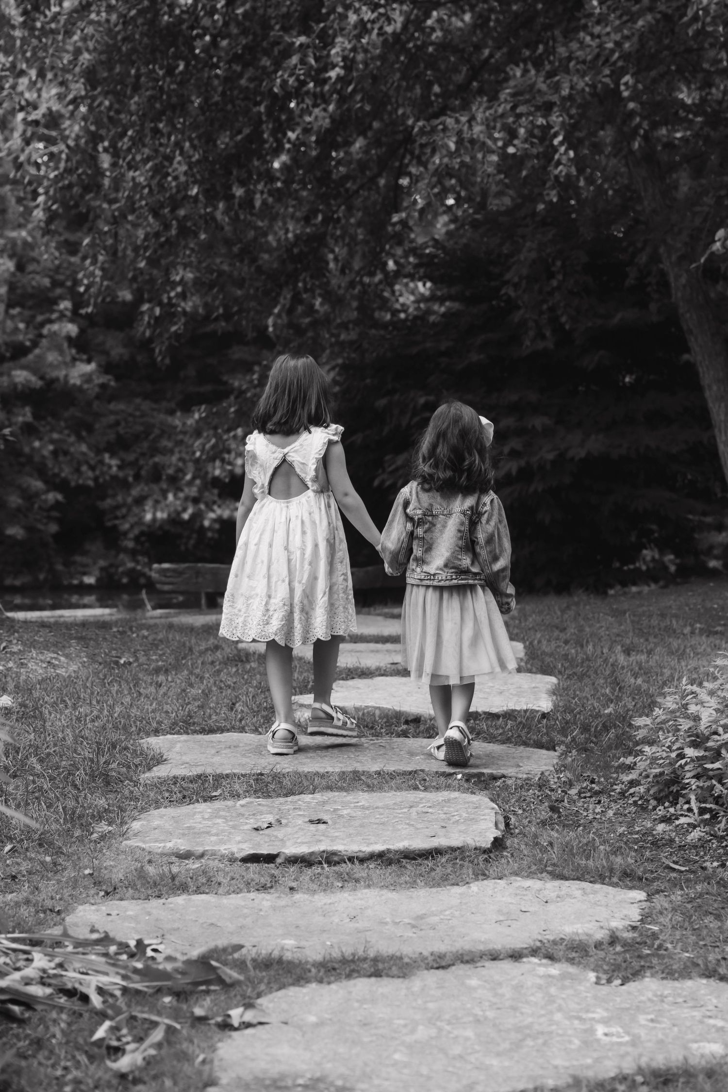Black and white photo of two young girls holding hands walking up stone steps in a garden.
