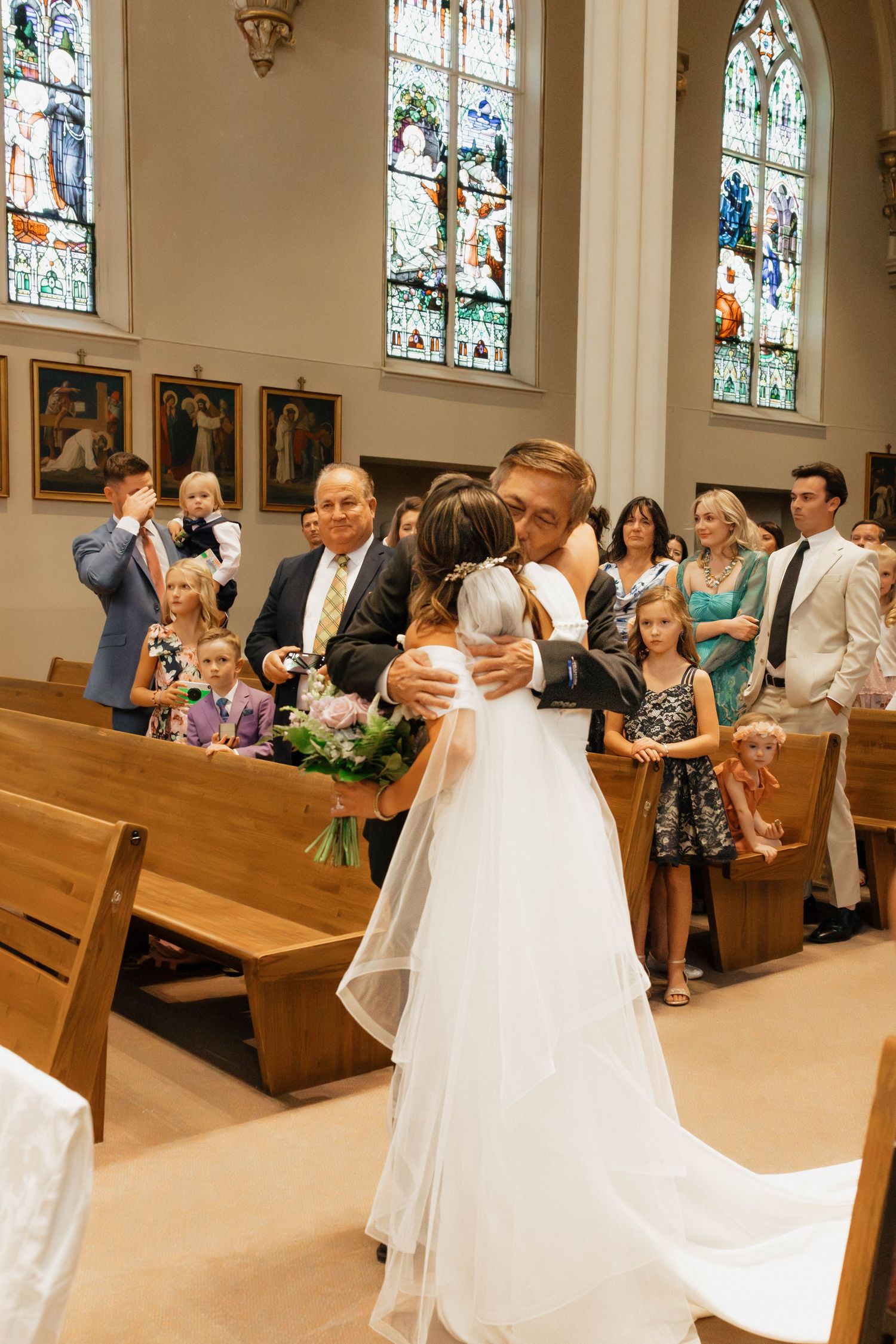 Bride and groom share first embrace at church altar surrounded by wedding guests in wooden pews.