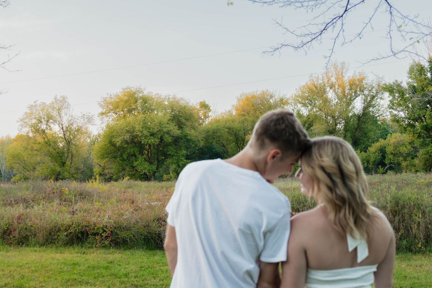 Couple standing together in a lush green park, viewed from behind, sharing an intimate moment.