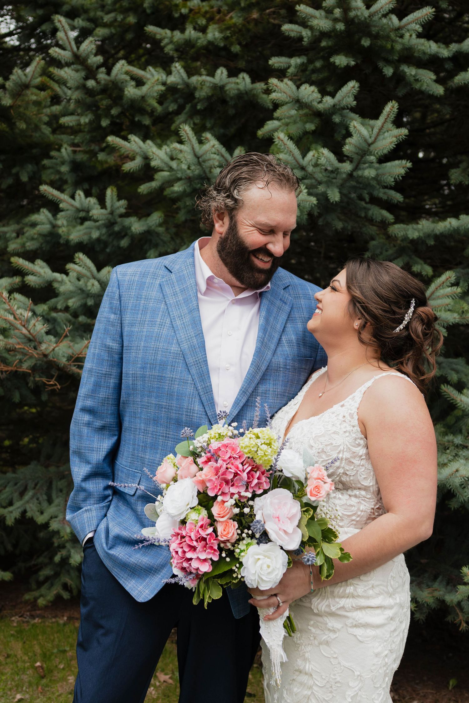 Smiling bride and groom in blue blazer share a joyful moment holding a colorful floral bouquet.