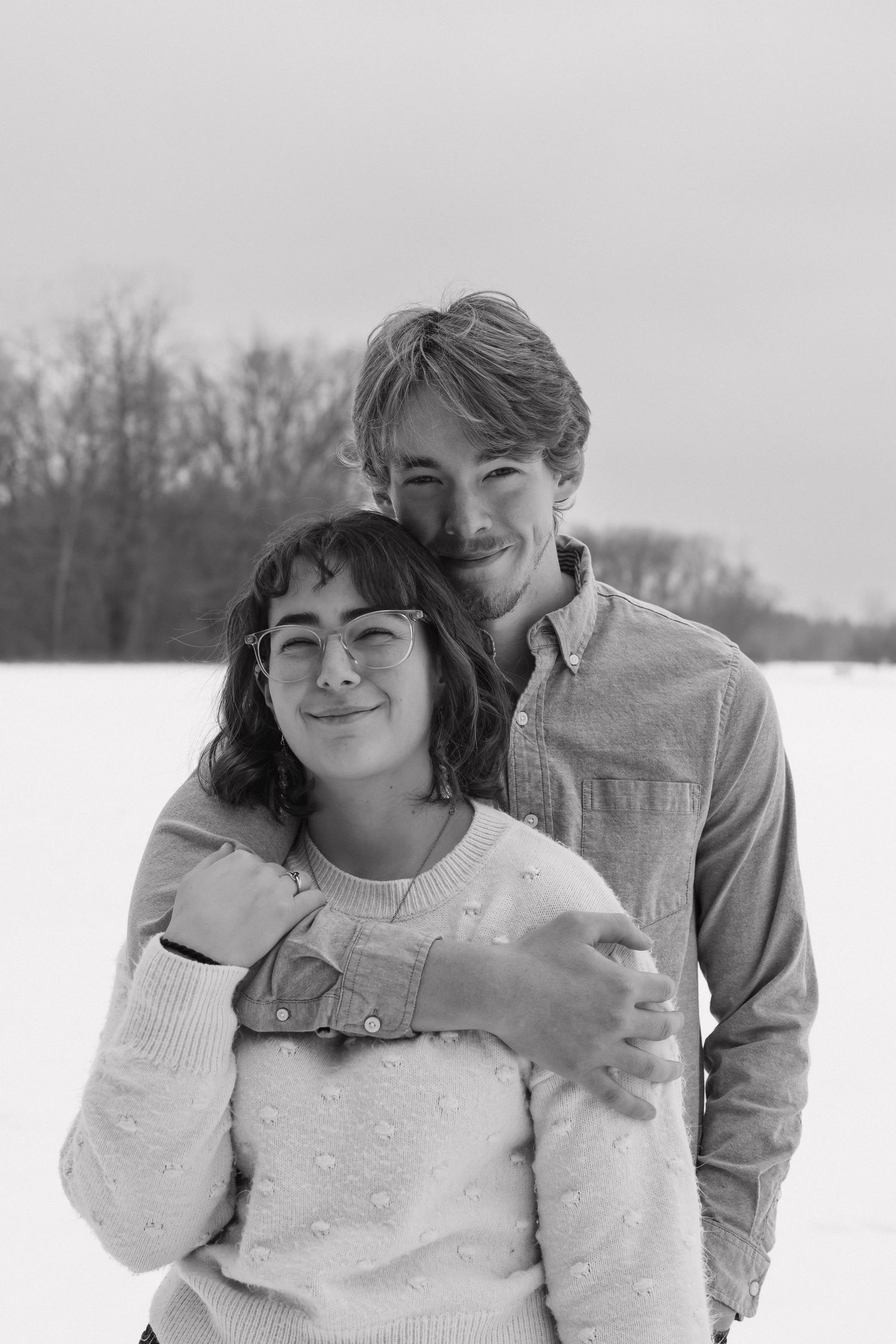 Black and white portrait of a young couple posing together in a snowy winter landscape.