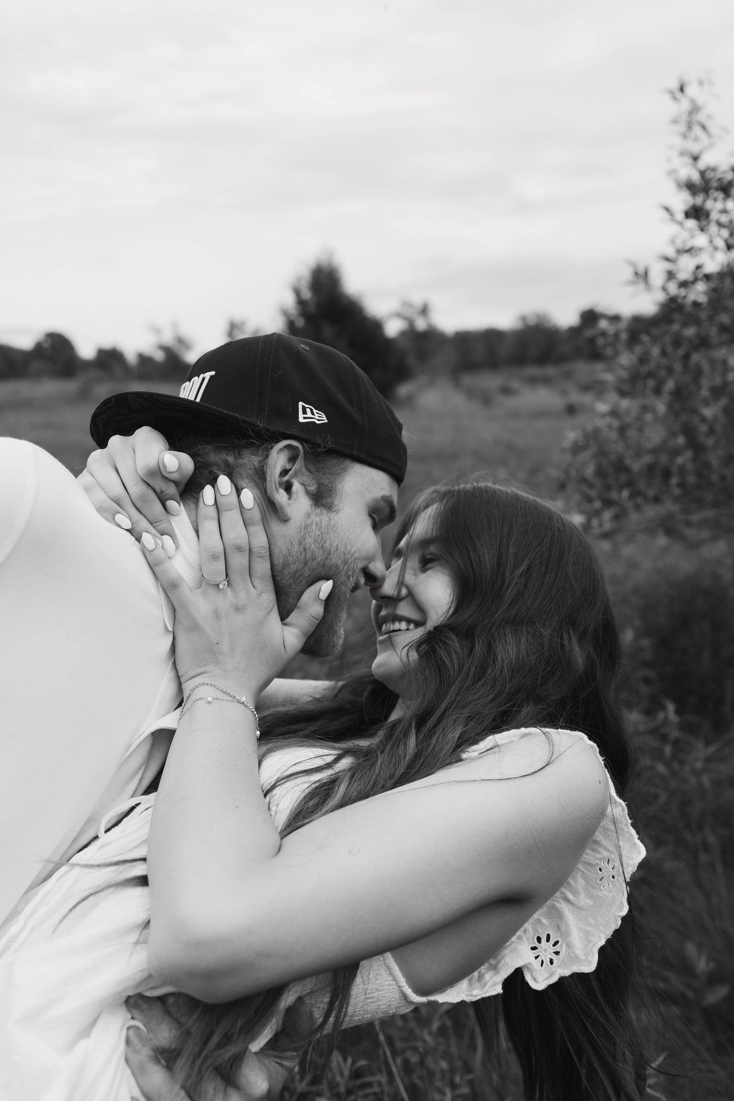 Black and white romantic photo of laughing couple nearly kissing outdoors in a natural field setting.