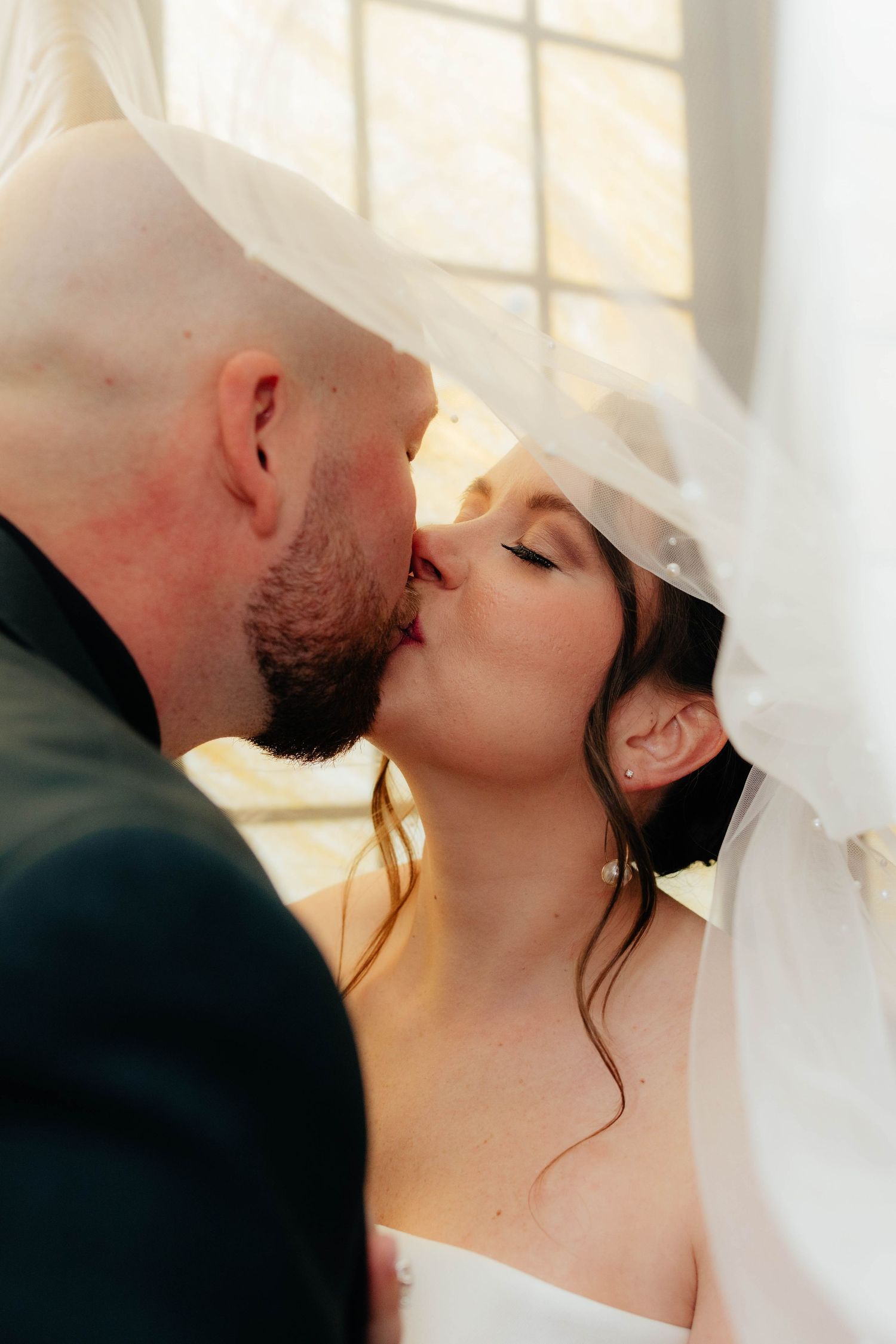 Close-up of bride and groom sharing a romantic kiss beneath the bridal veil.