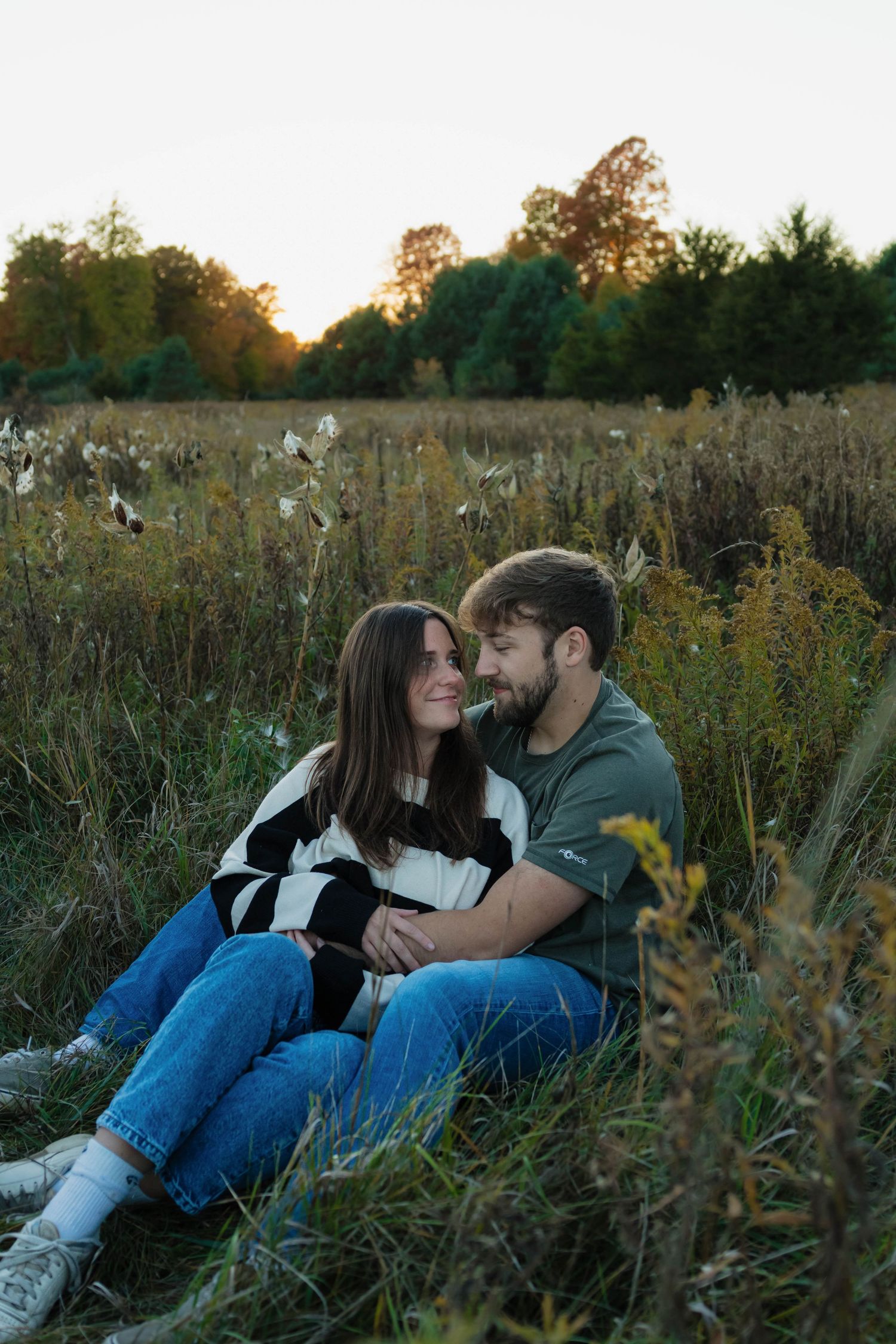 Couple sitting closely together in a scenic autumn meadow during a warm and glowing sunset.
