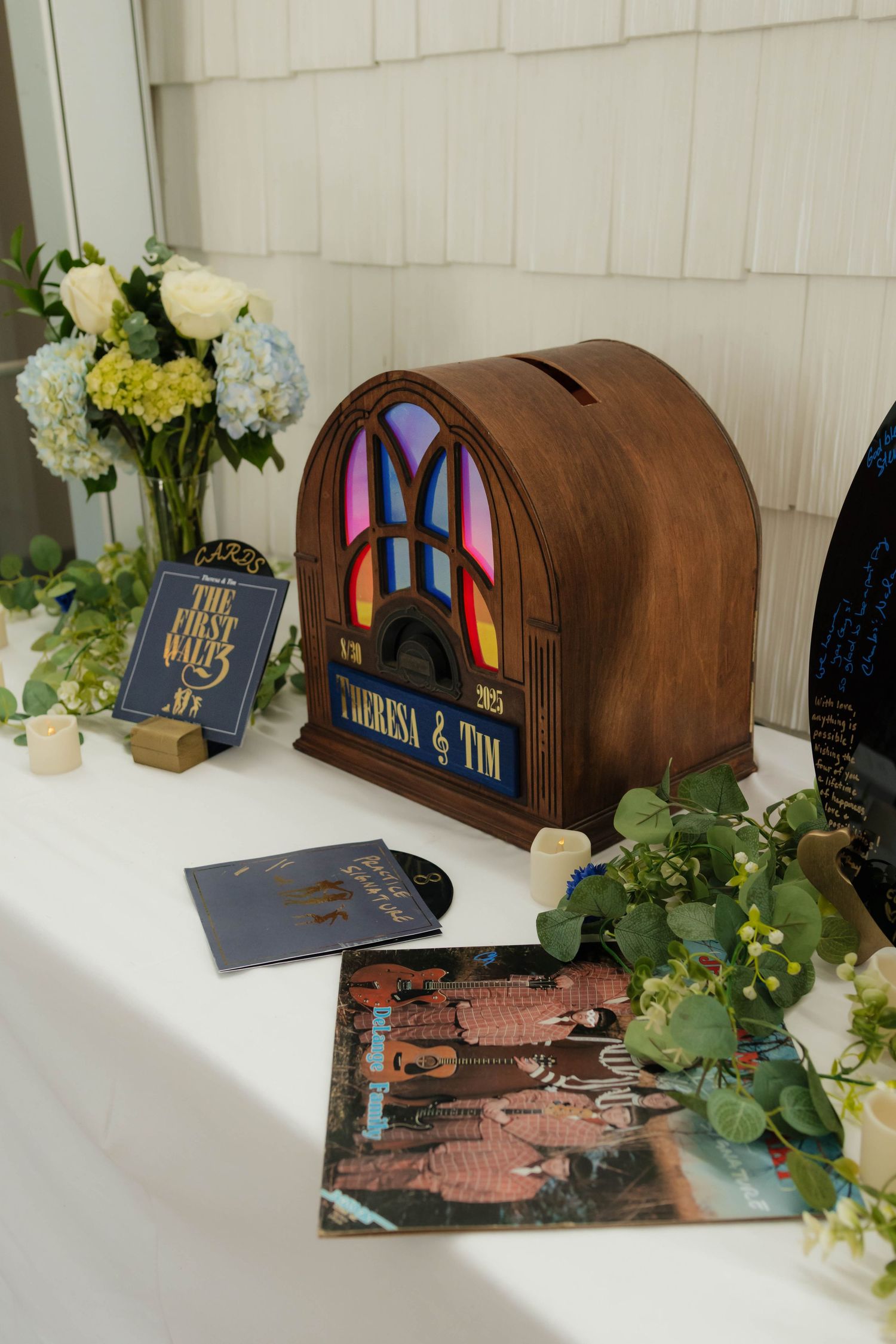 Wooden radio-shaped card box engraved with Theresa and Tim displayed on wedding reception table.