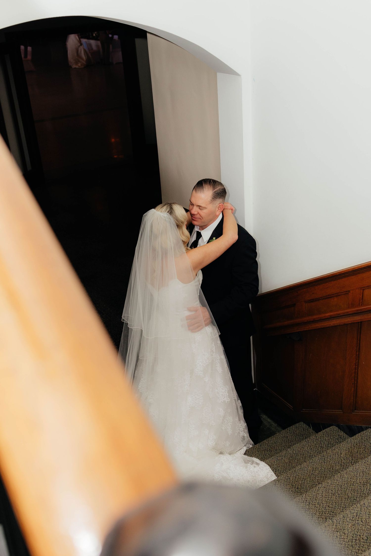 Emotional father-daughter embrace on staircase before wedding ceremony in classic venue.