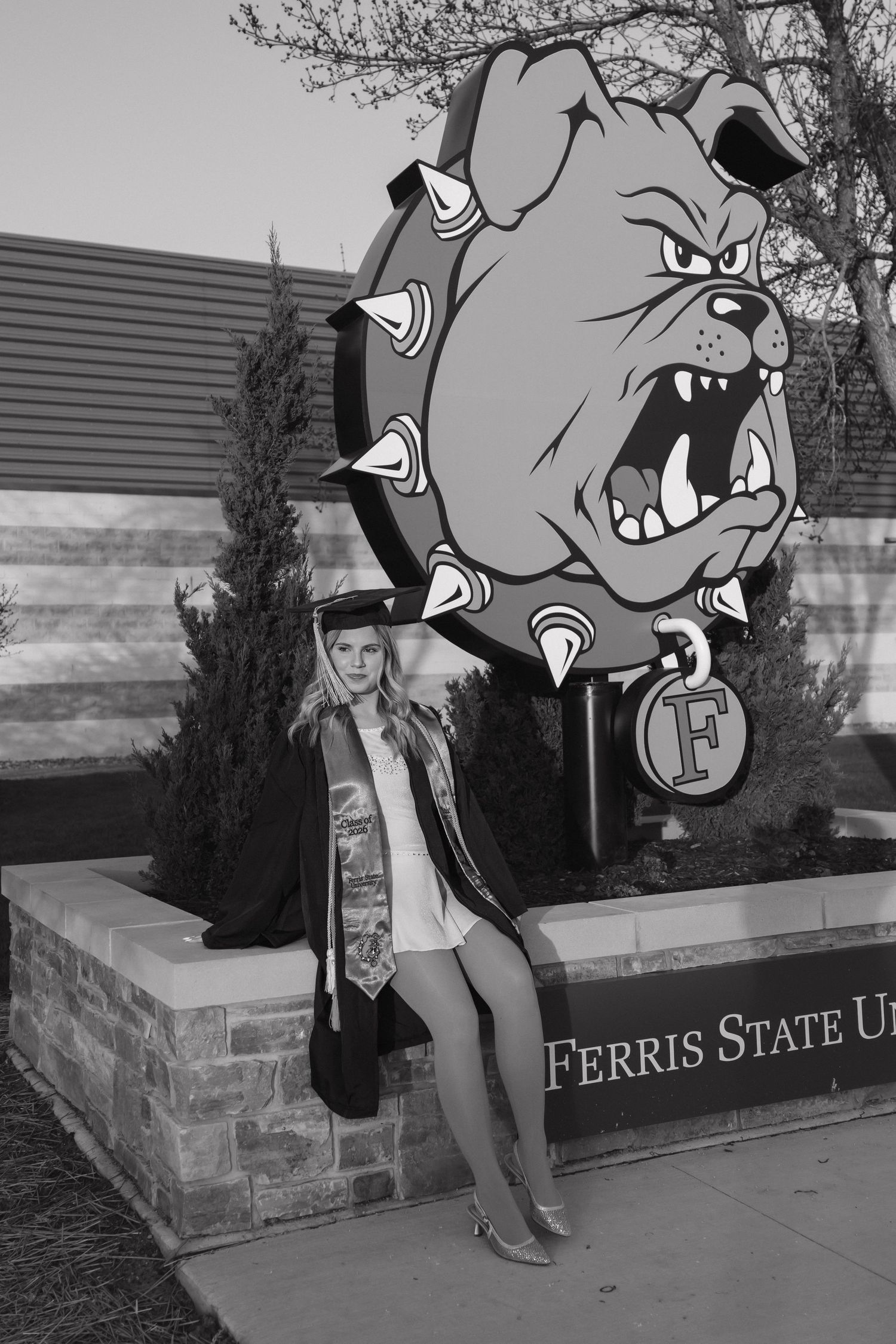 Black and white photo of graduate posing beside Ferris State University bulldog mascot sign.