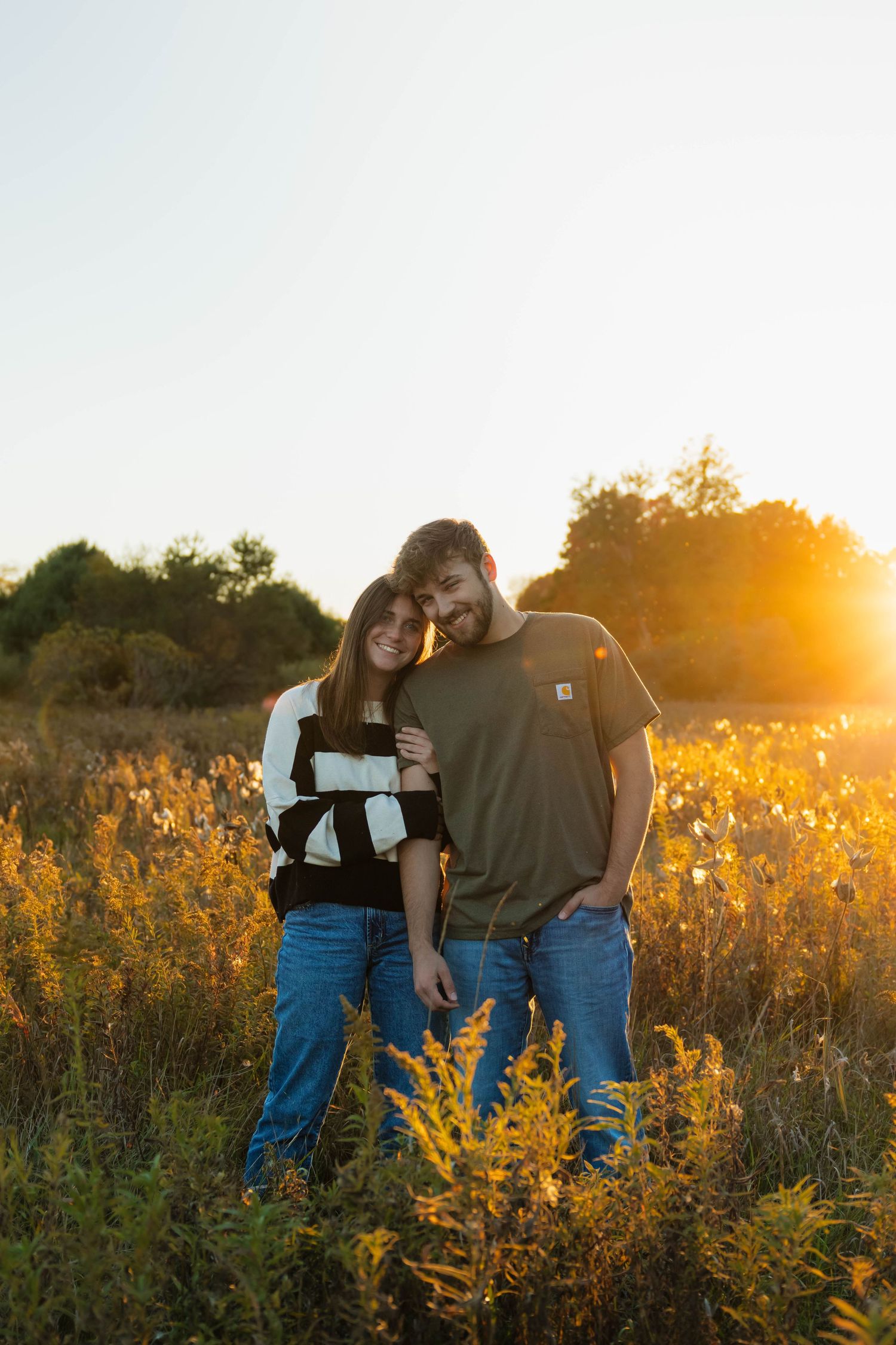 Couple embracing in a golden field at sunset with warm sunlight glowing behind them.
