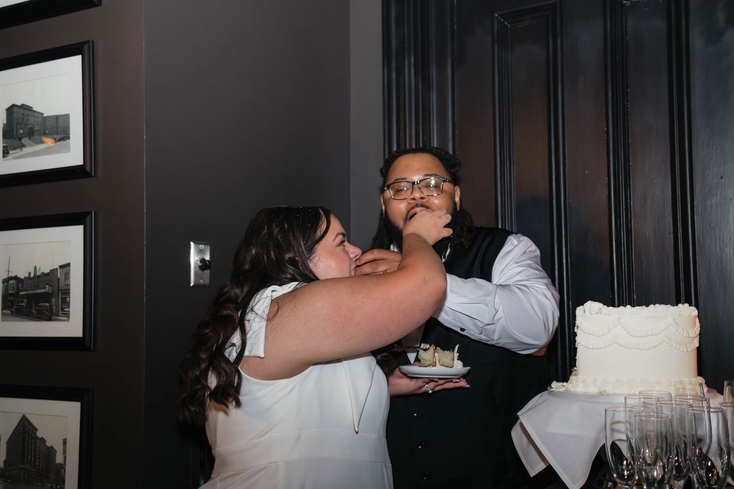Bride feeds groom wedding cake during fun cake cutting ceremony at elegant reception.