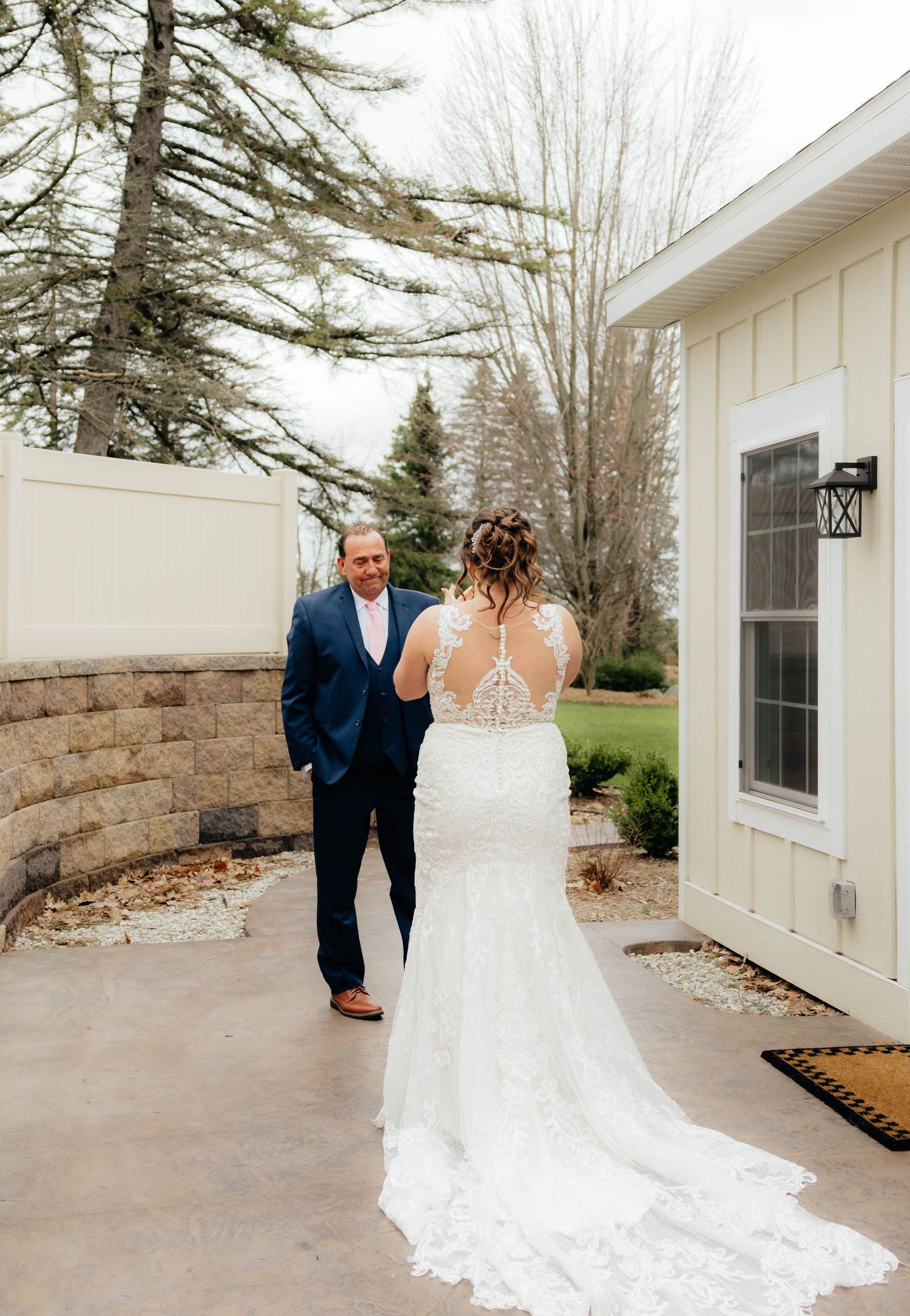 Father in navy suit turning to see bride in lace gown during outdoor first look reveal.