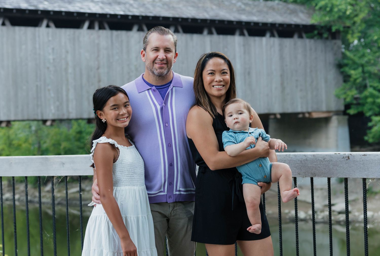 Smiling family with two children posing near a historic covered bridge.