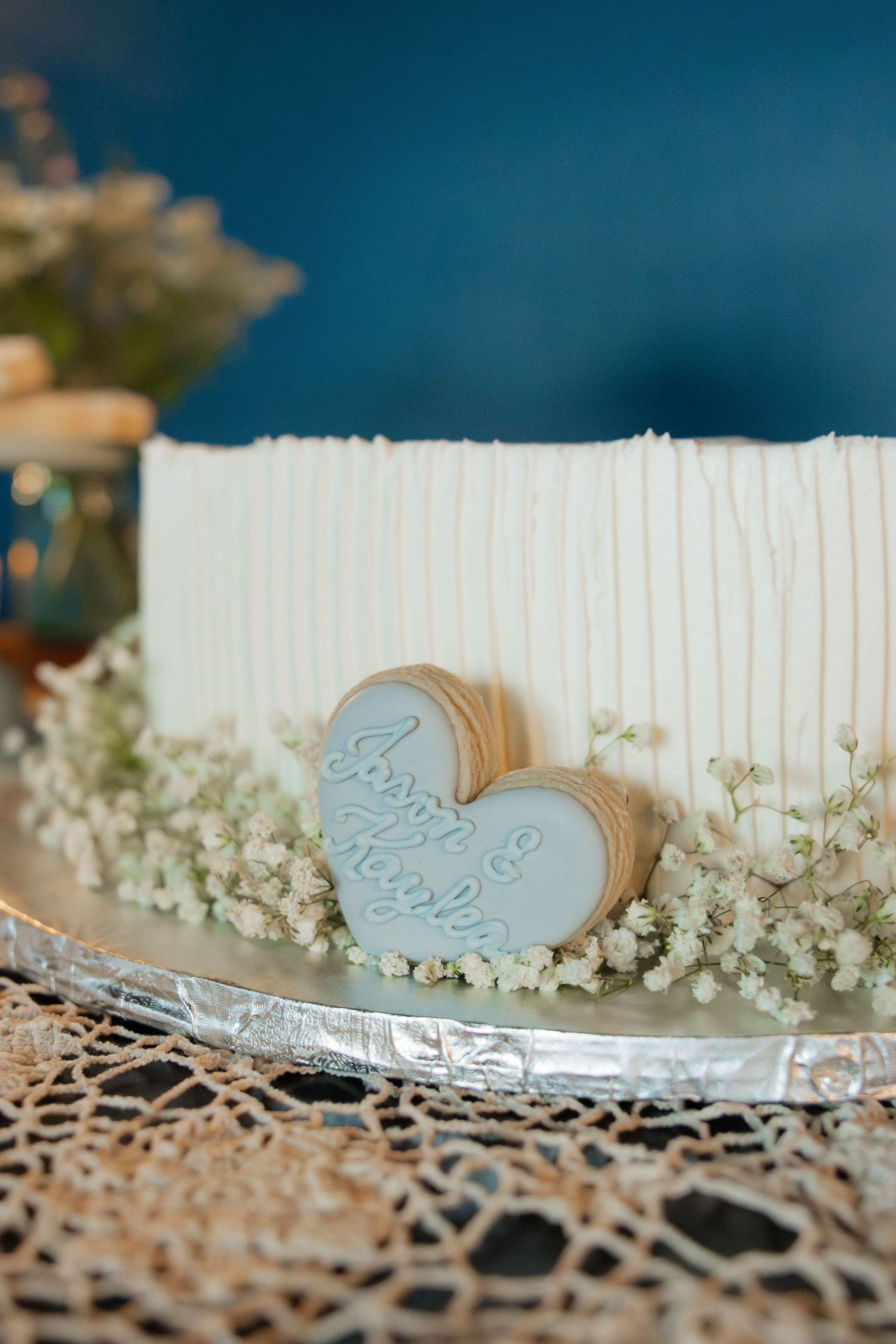 White textured wedding cake decorated with baby's breath and a light blue heart-shaped topper with couple's names.