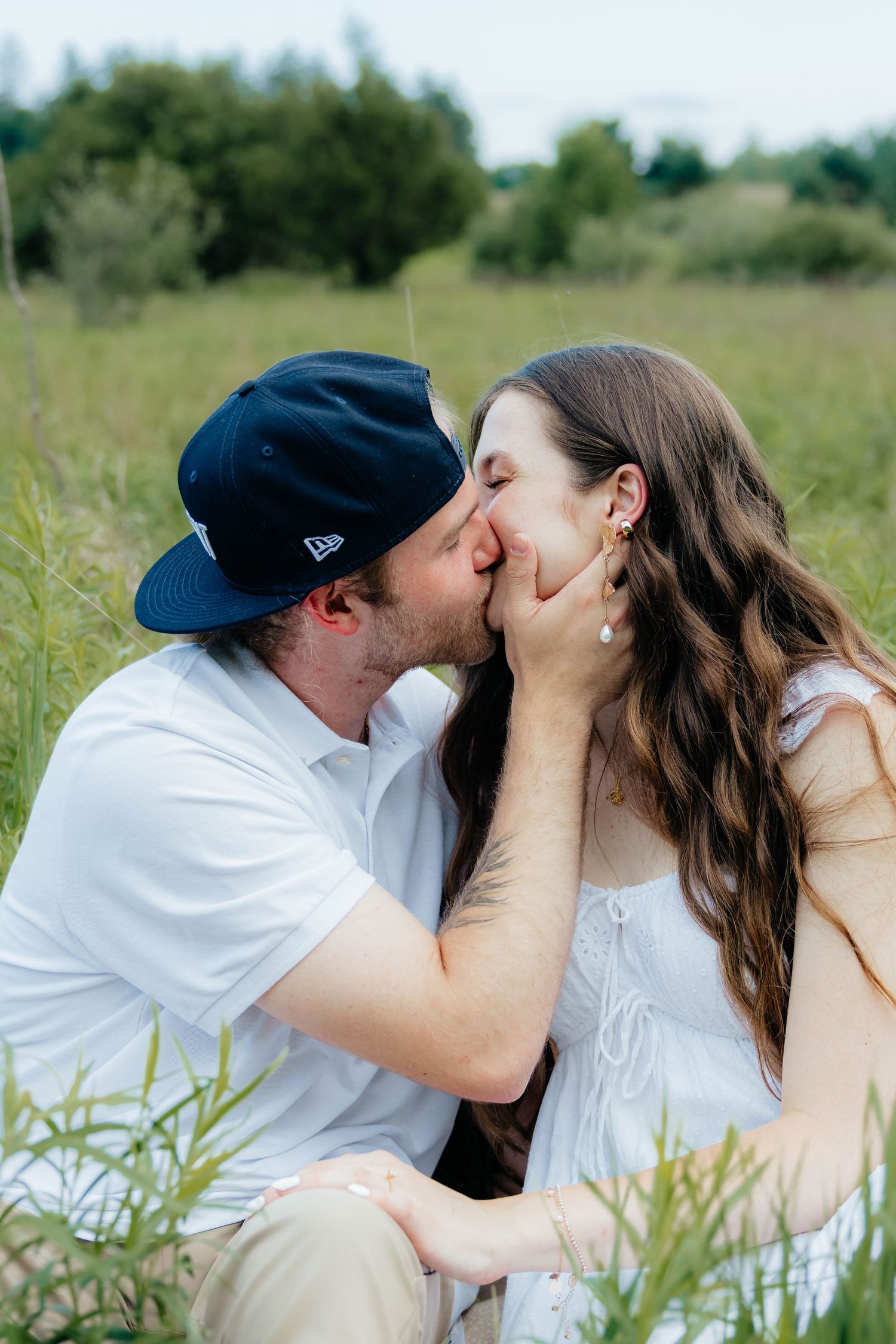 Couple sharing a tender kiss while sitting in a green field surrounded by nature.
