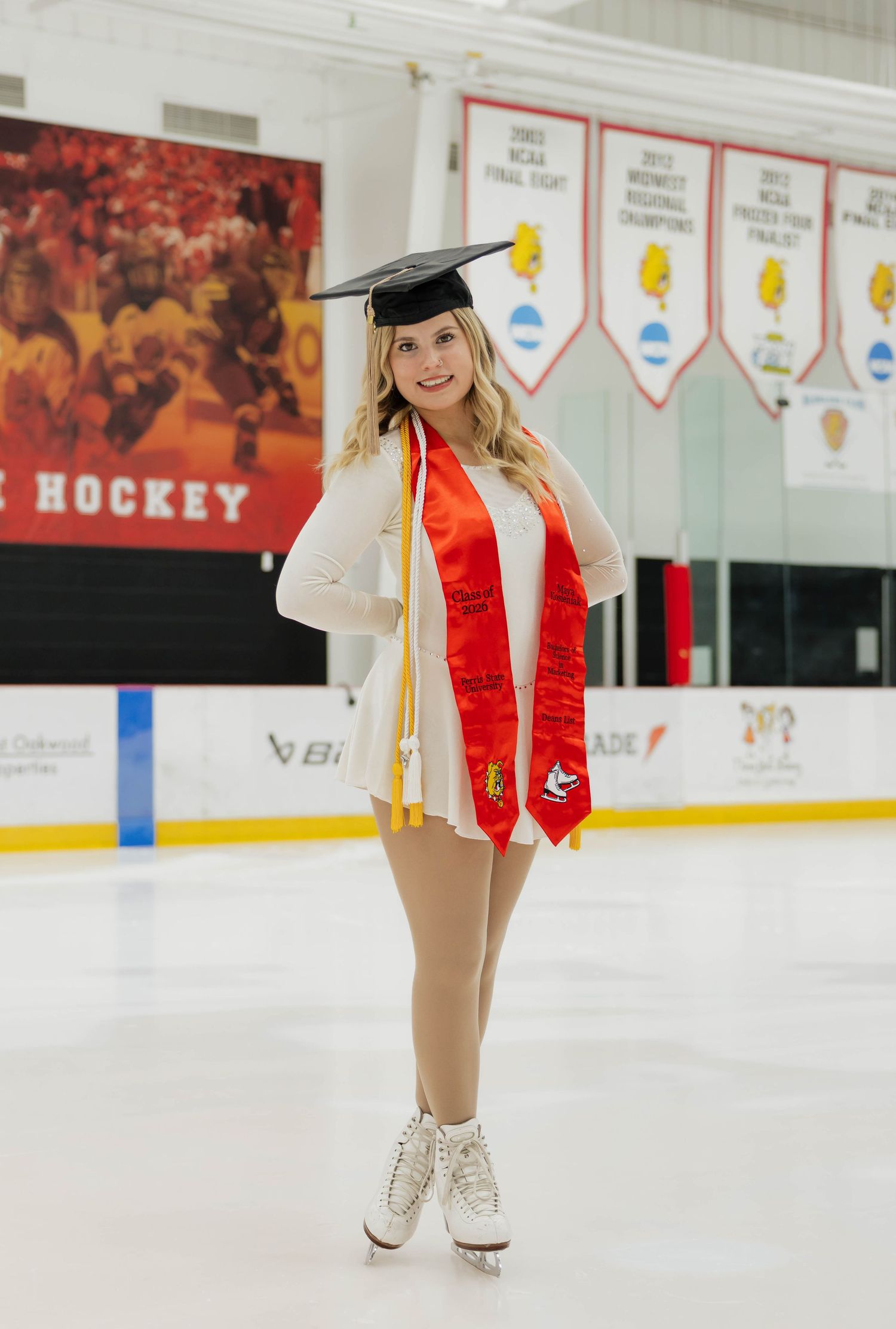 Graduate in mortarboard and red stole posing on ice rink wearing white figure skates.