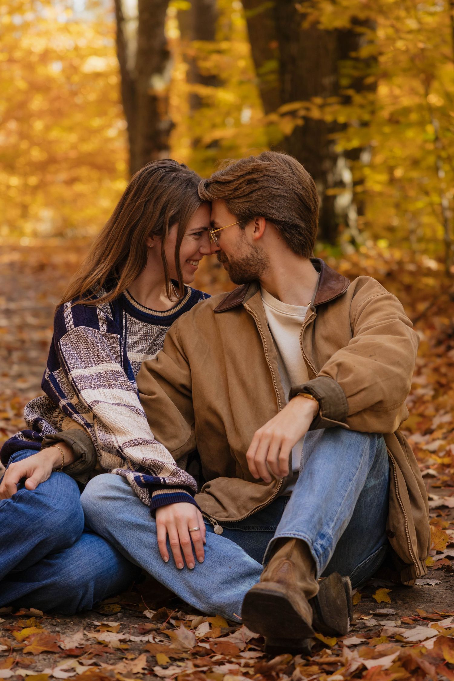 Couple sharing a romantic moment sitting among autumn leaves in a colorful fall forest.