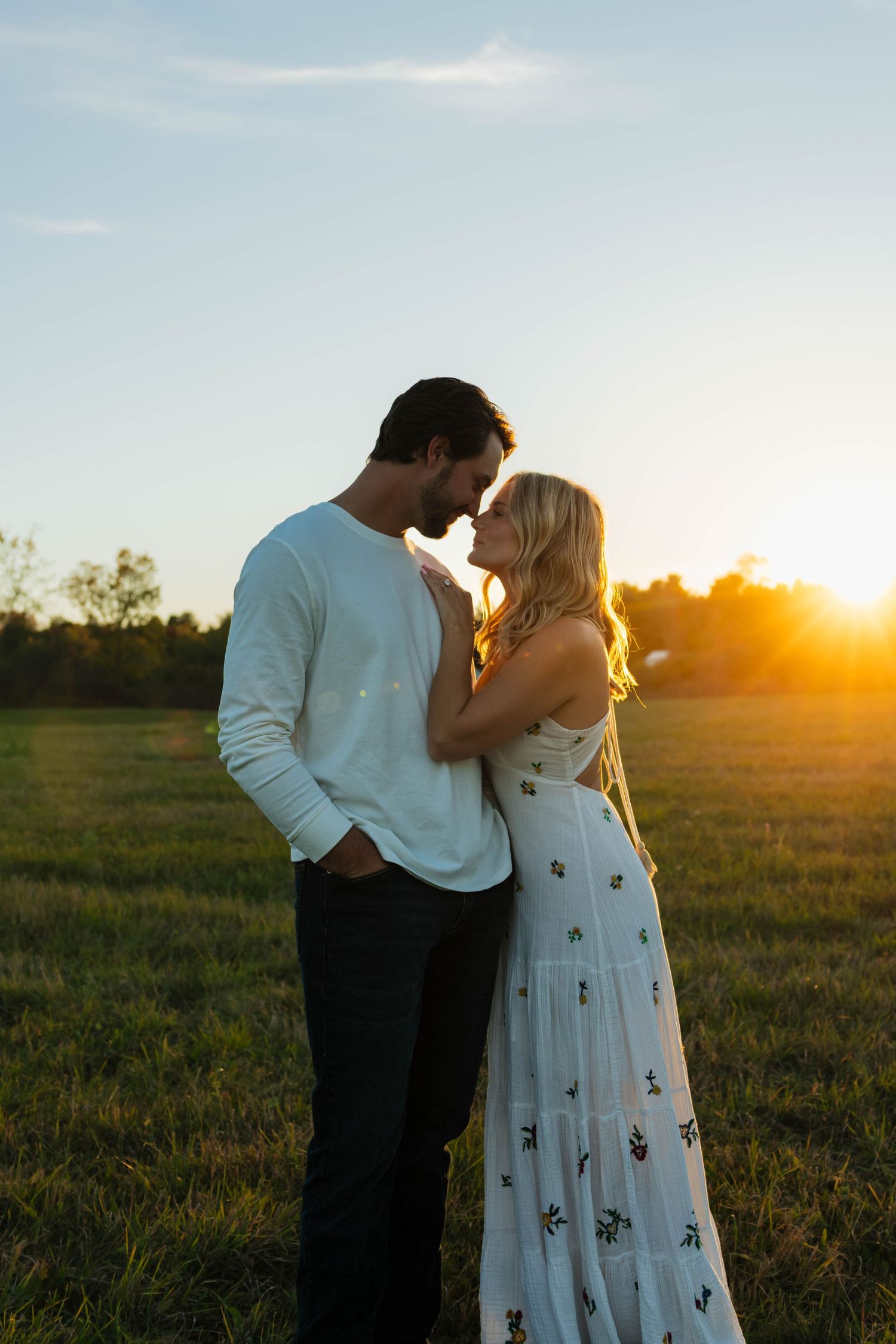 Couple sharing a tender moment at golden hour sunset in a beautiful open green field.