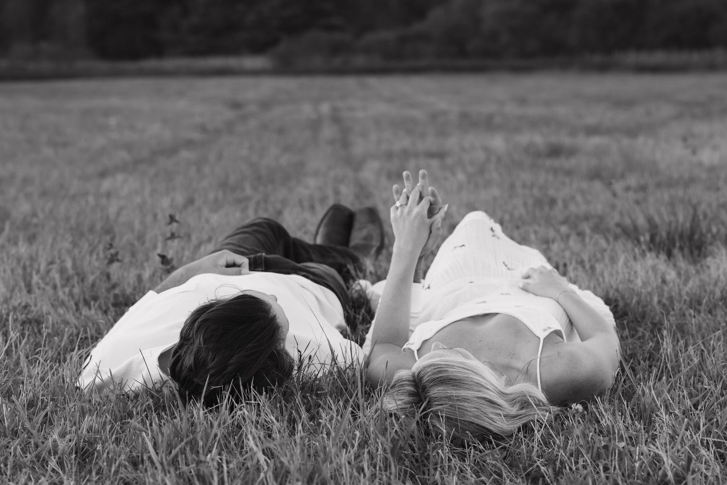 Black and white photo of a couple lying side by side in a grassy field looking up.