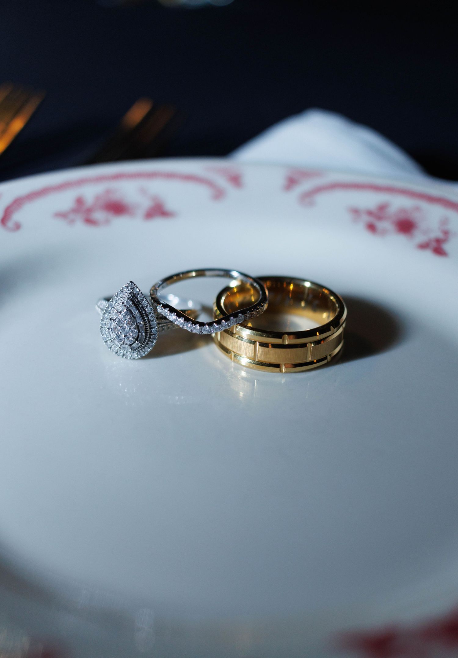 Wedding rings displayed on decorative plate, featuring diamond halo engagement ring and gold bands.