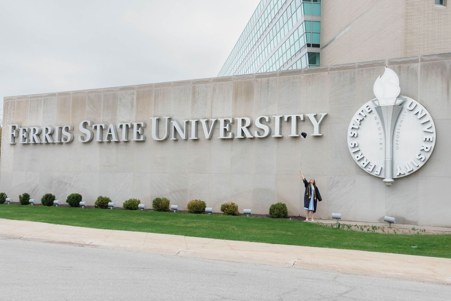 Two graduates posing in front of Ferris State University sign on campus.