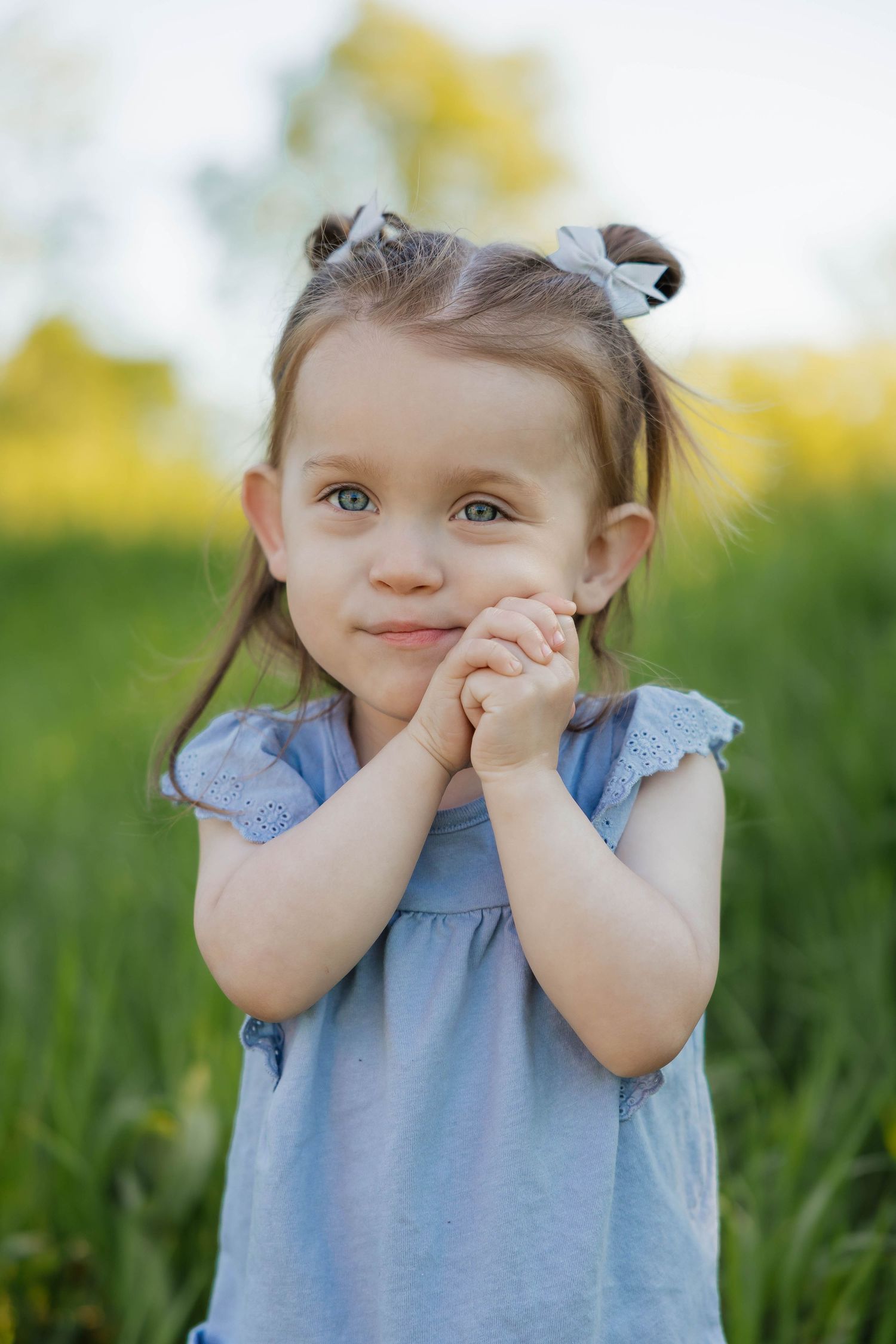 Adorable little girl with pigtails clasping her hands together smiling in a sunny green field.