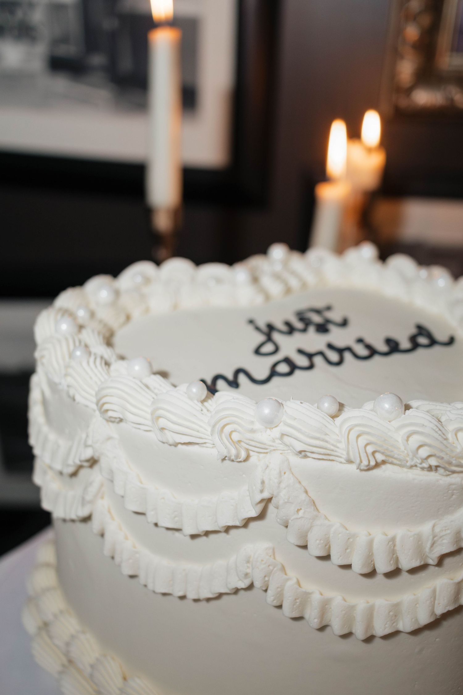 Elegant white wedding cake decorated with ruffled frosting and 'just married' written in black icing.