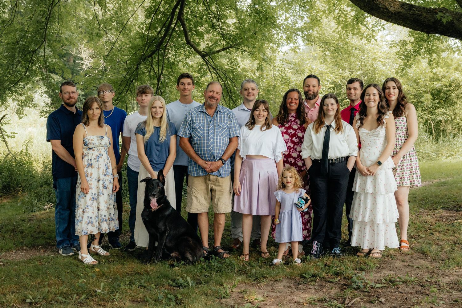 Large extended family group portrait standing outdoors under a large willow tree.