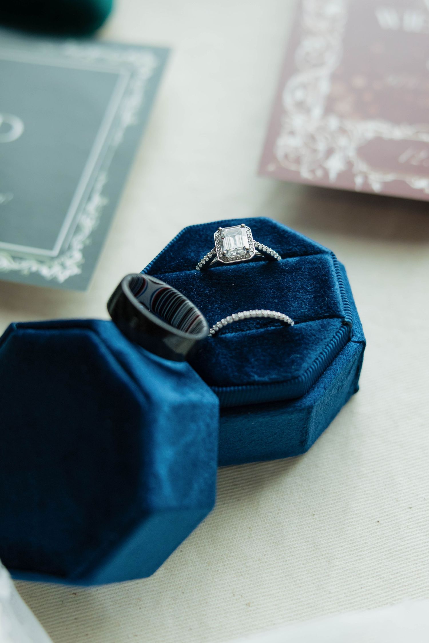 Diamond engagement ring and black wedding band displayed in an octagonal navy blue velvet ring box.
