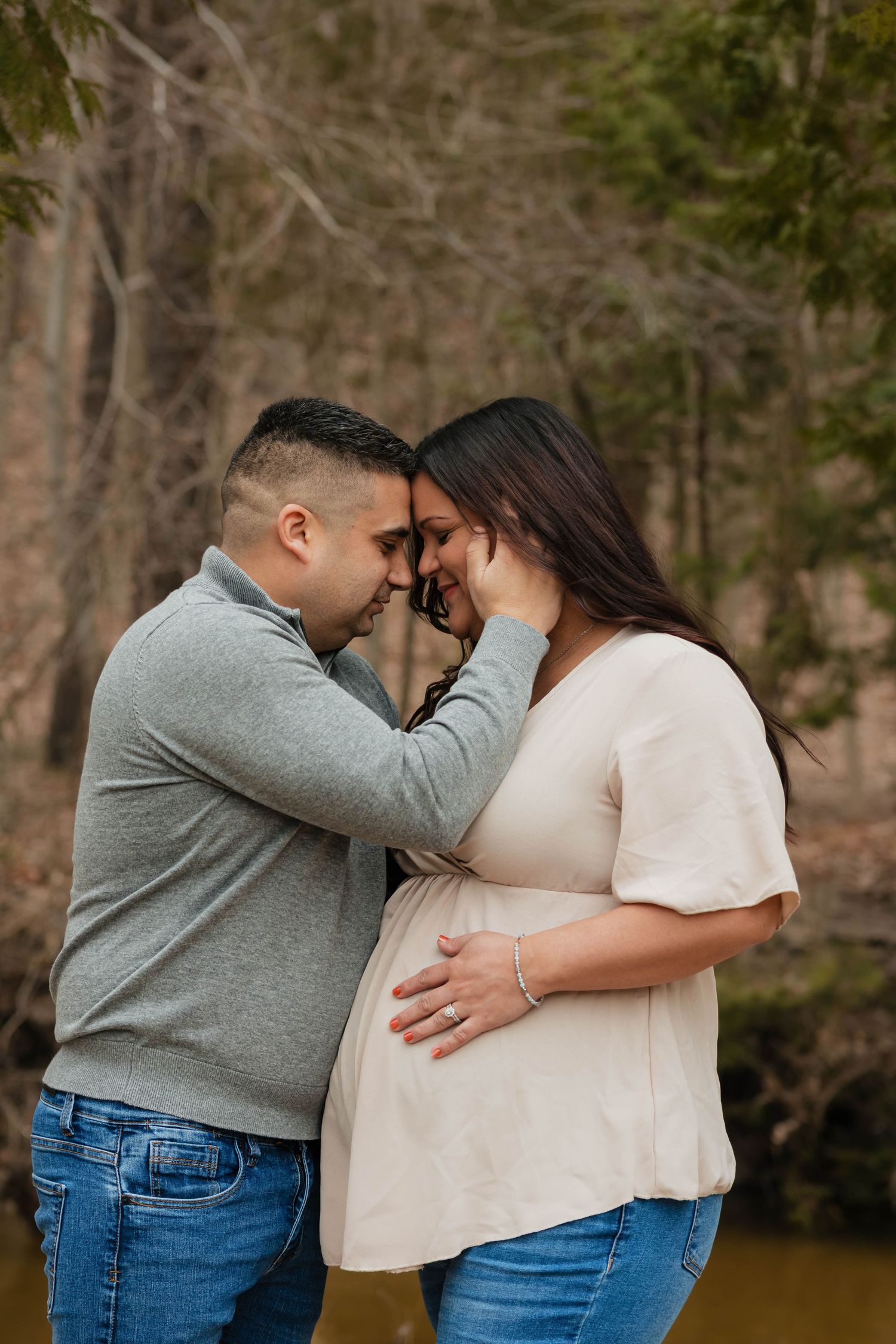 Expectant couple tenderly touching foreheads while cradling baby bump in an autumn forest setting.