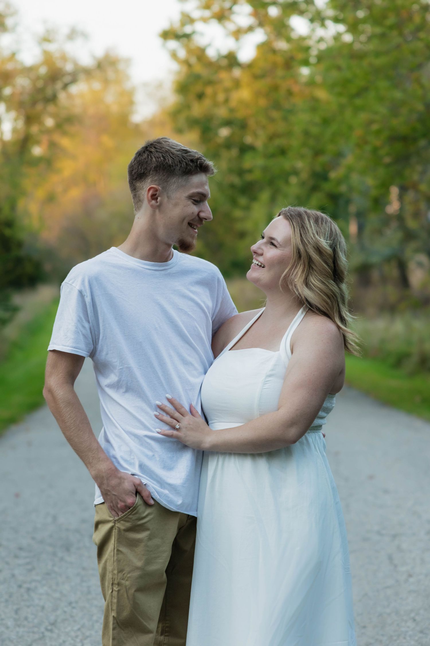 Happy couple smiling at each other on a gravel path surrounded by autumn foliage.