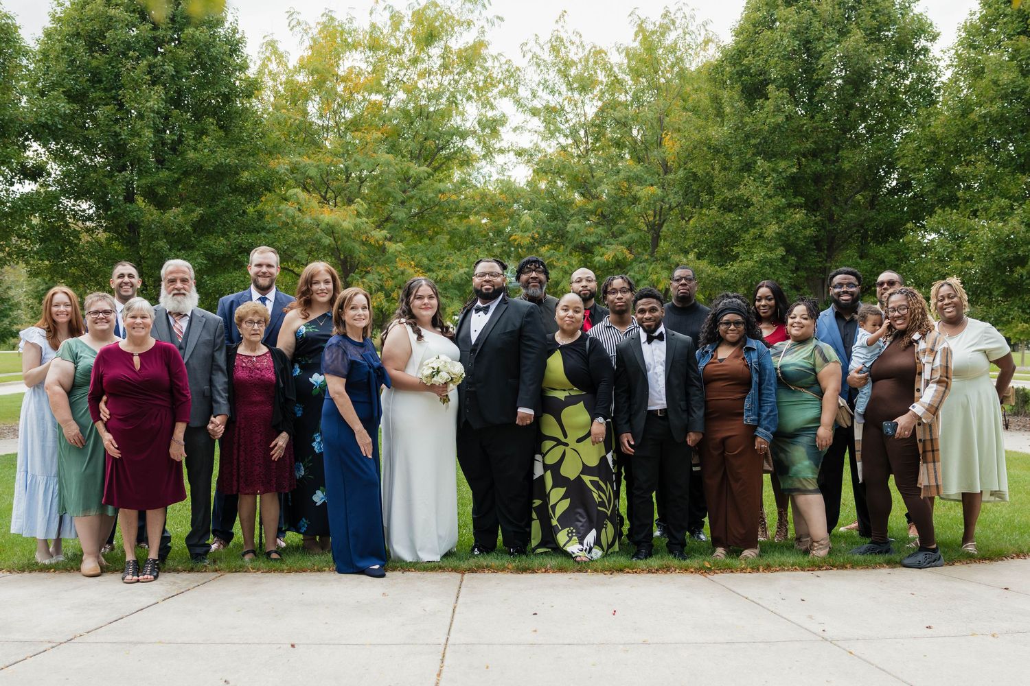 Large wedding party group photo outdoors with bride and groom surrounded by family and friends.