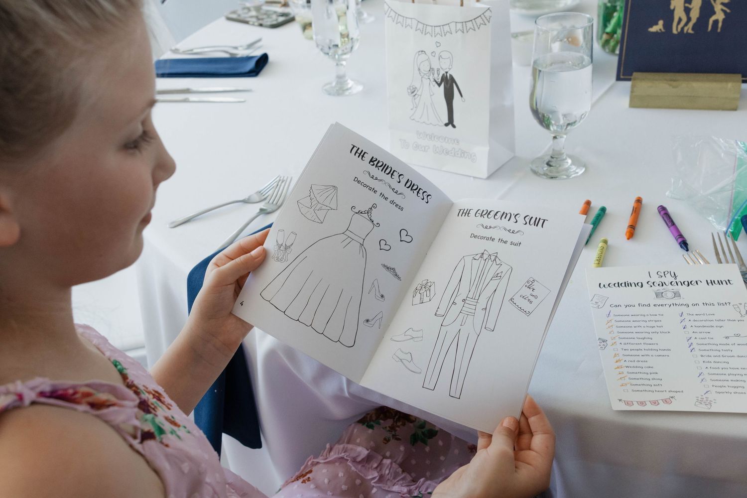 Young girl reads wedding activity coloring book at decorated reception table with crayons nearby.