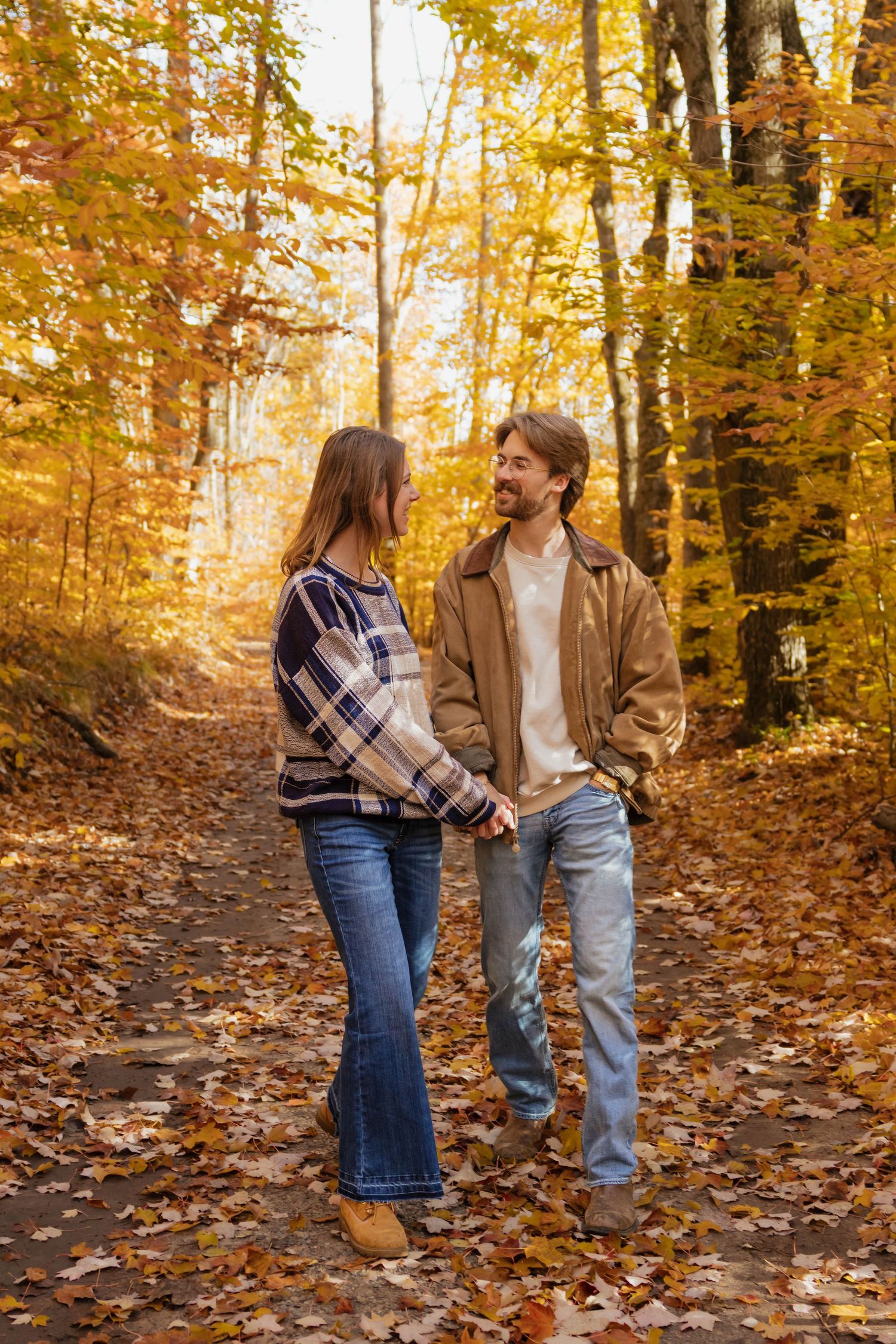 Happy couple holding hands and smiling on a scenic autumn forest path with golden foliage.