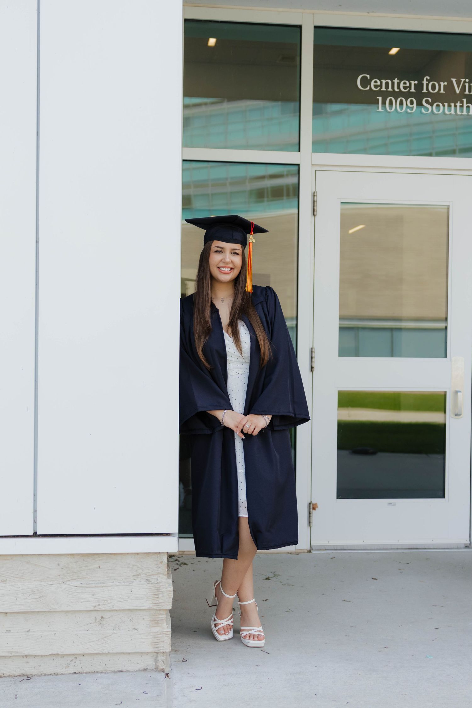 Graduate in navy cap and gown smiling outside the Center for Visual Arts building.