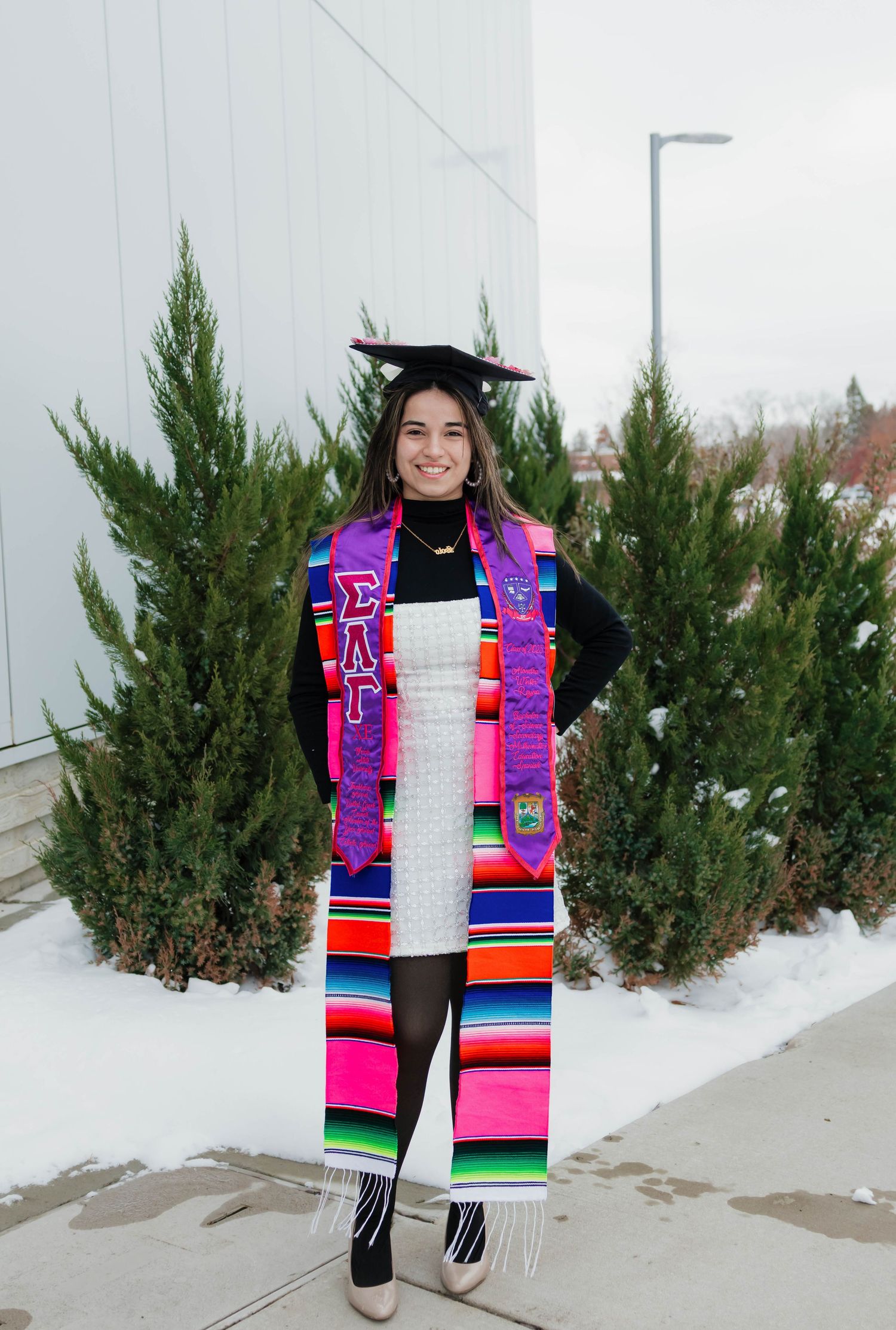 Graduate smiling in cap and Sigma Lambda Gamma stole with colorful serape in snowy outdoor setting.