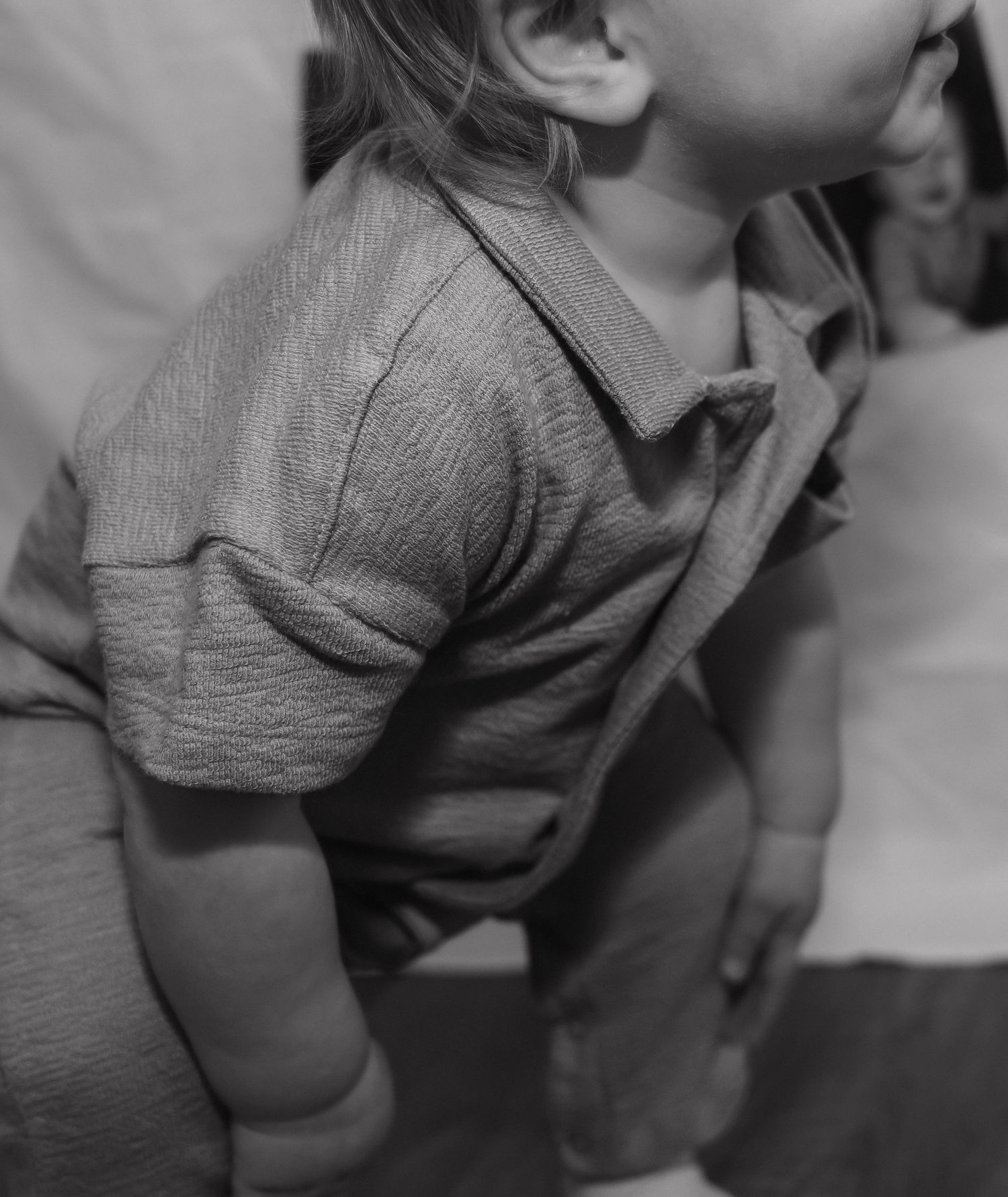 Black and white close-up of a toddler in a textured short-sleeve shirt being held by an adult.