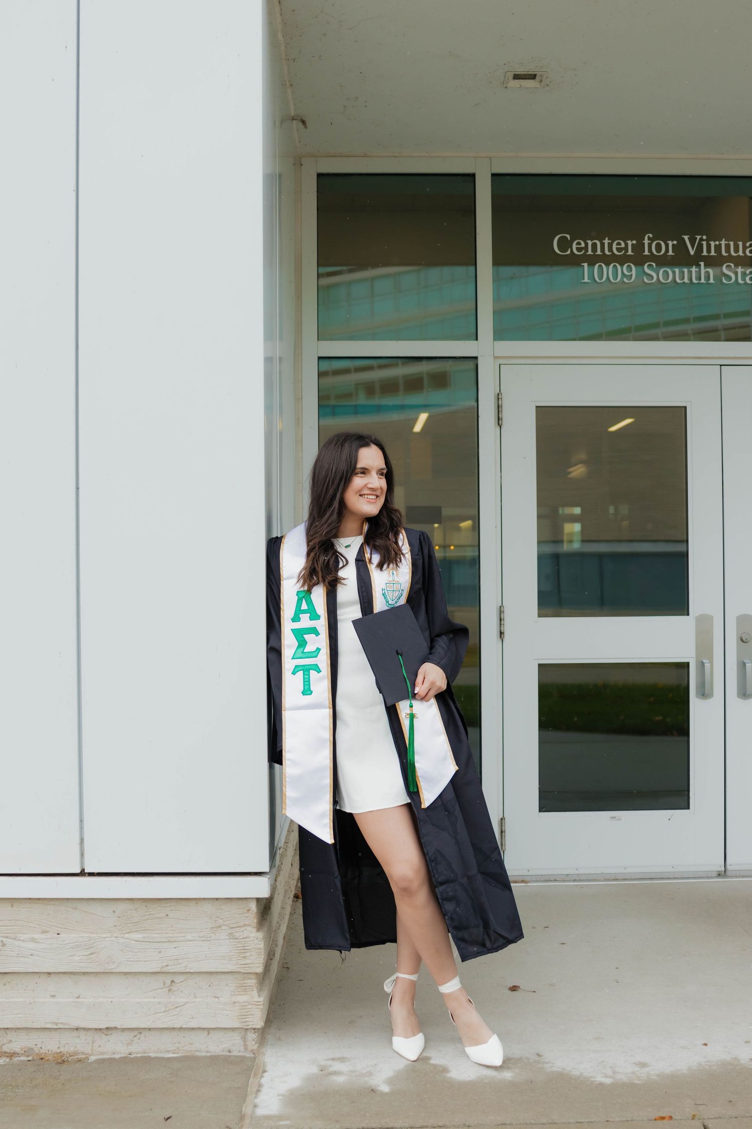 Graduate in cap and gown with Alpha Sigma Tau stole posing outside Center for Virtual Learning.