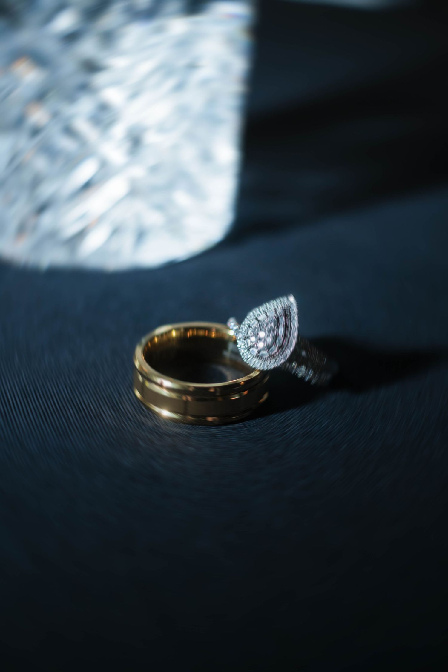 Pear-shaped diamond engagement ring paired with gold wedding band on dark fabric surface.