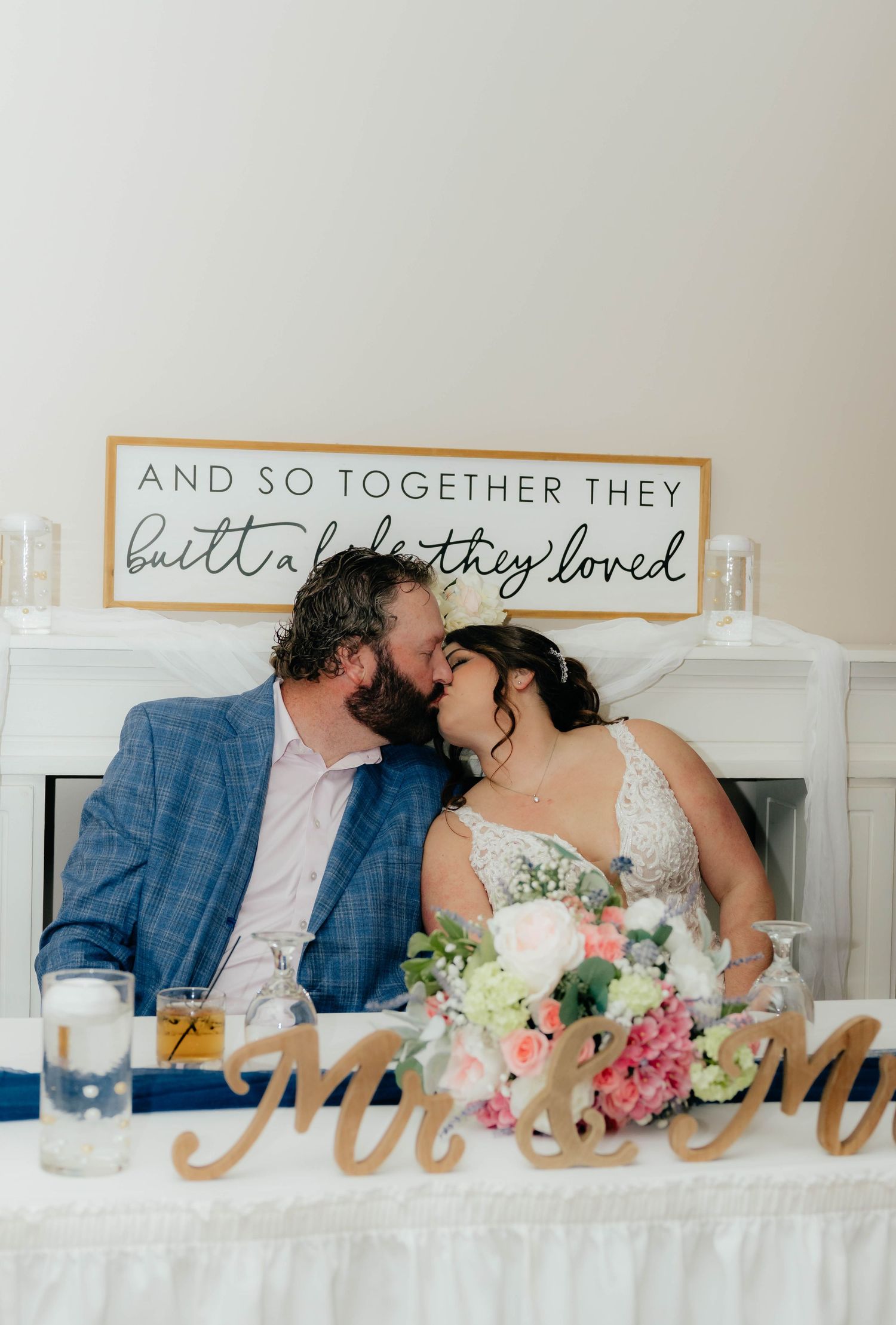 Newlyweds kiss at sweetheart table beneath sign reading and so together they built a life they loved.
