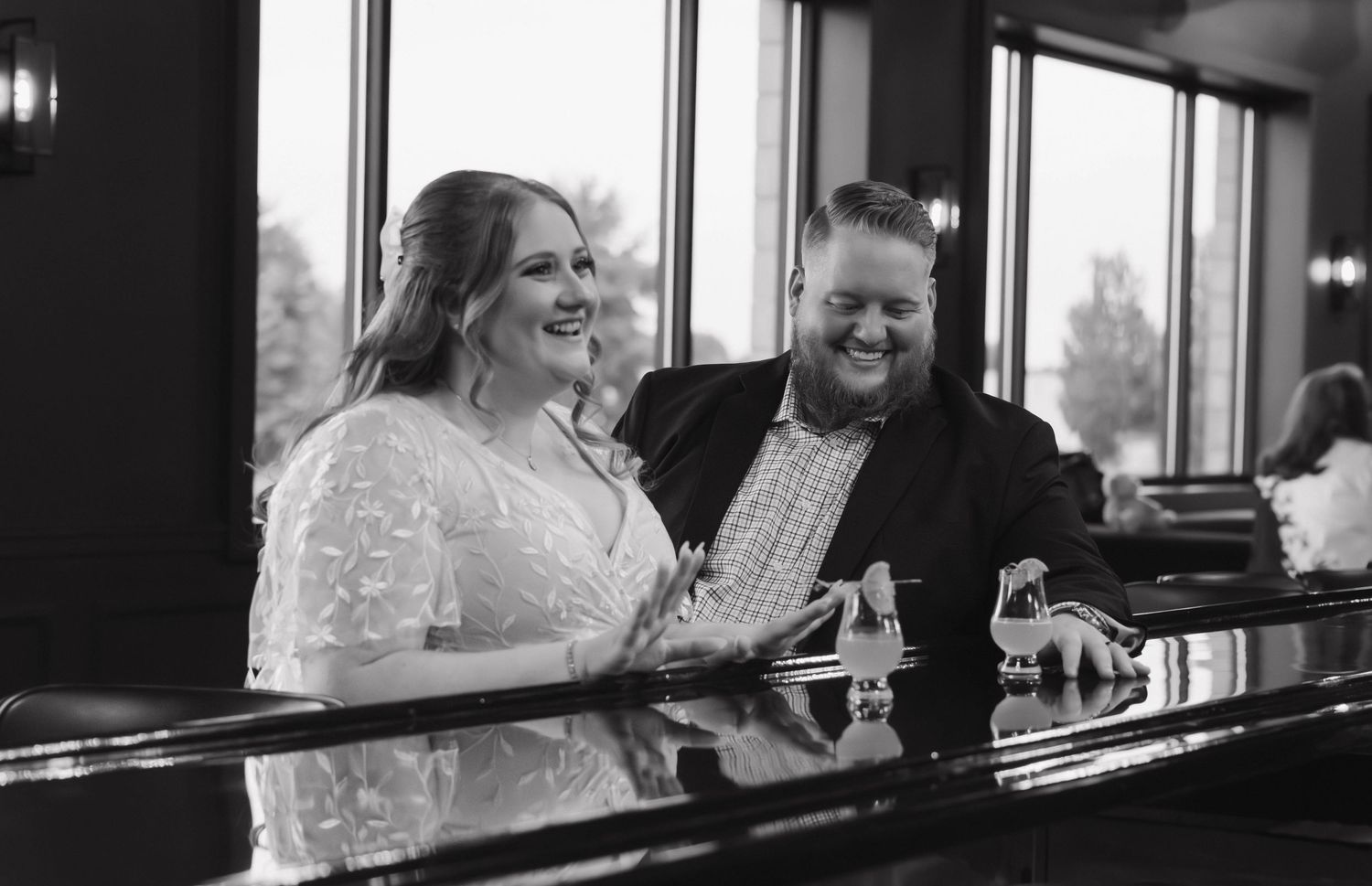Bride and groom laugh together at a bar in a candid black and white wedding photo.